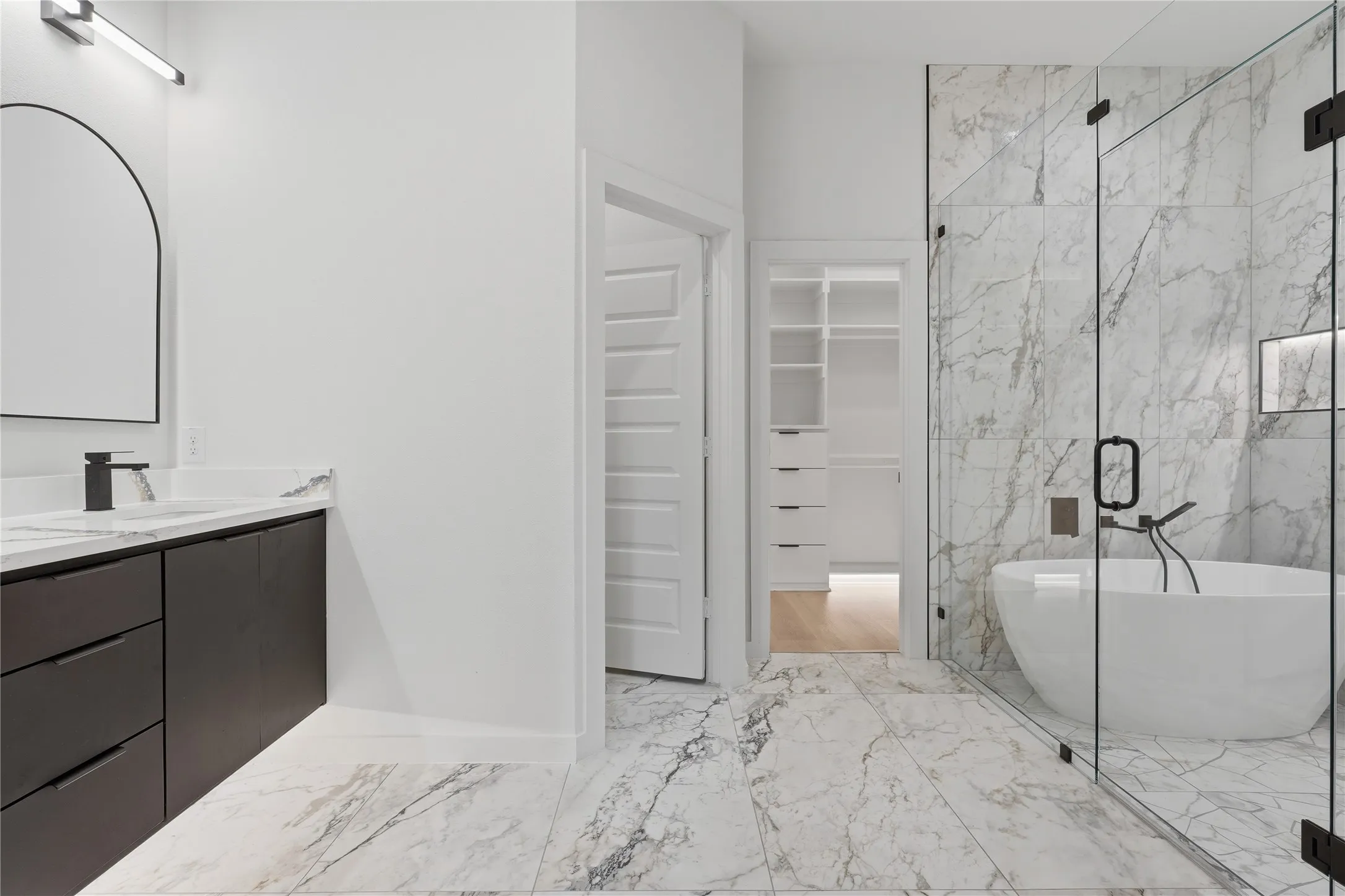 Bathroom featuring a freestanding soaking tub, glass-enclosed shower, dual-tone vanity with a stone countertop, and custom closet shelving
