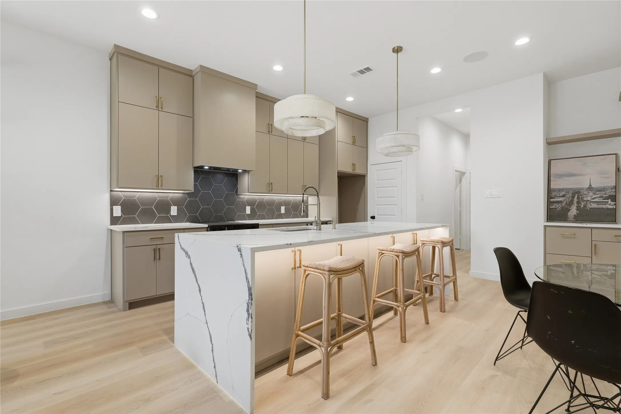 Spacious kitchen featuring a large waterfall island, light wood-finish flooring, recessed lighting, and a hexagon tile backsplash