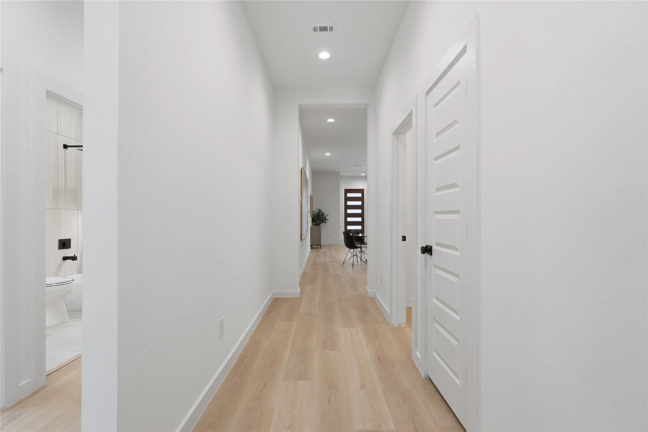 Recessed lighting, wood-finish flooring, white paneled doors with black hardware, and a modern dark wood entry door with horizontal lites