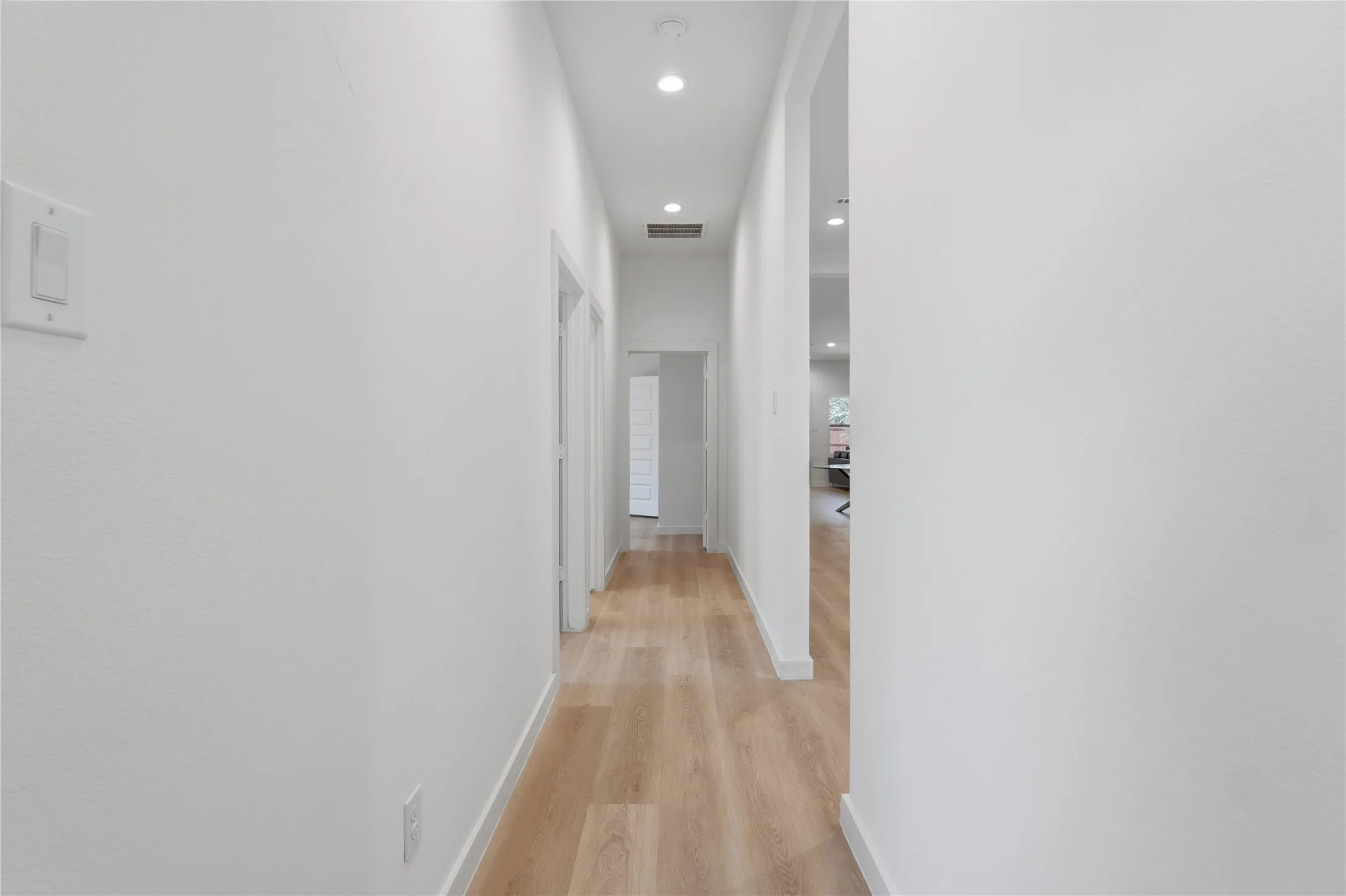 Recessed lighting illuminates the hall with wood-finish flooring