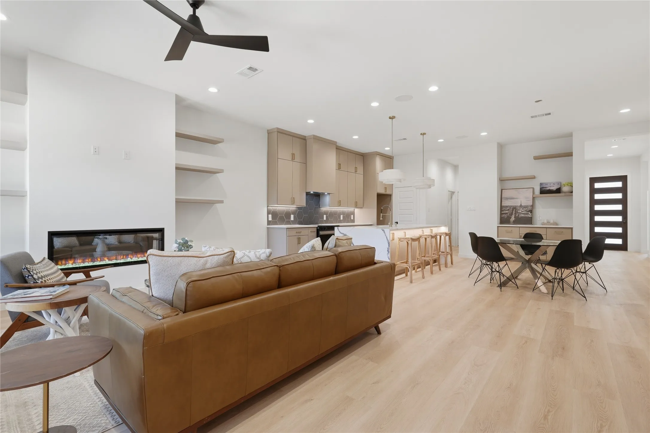 Open-concept living area featuring light wood-finish flooring, recessed lighting, a linear electric fireplace, and built-in shelving