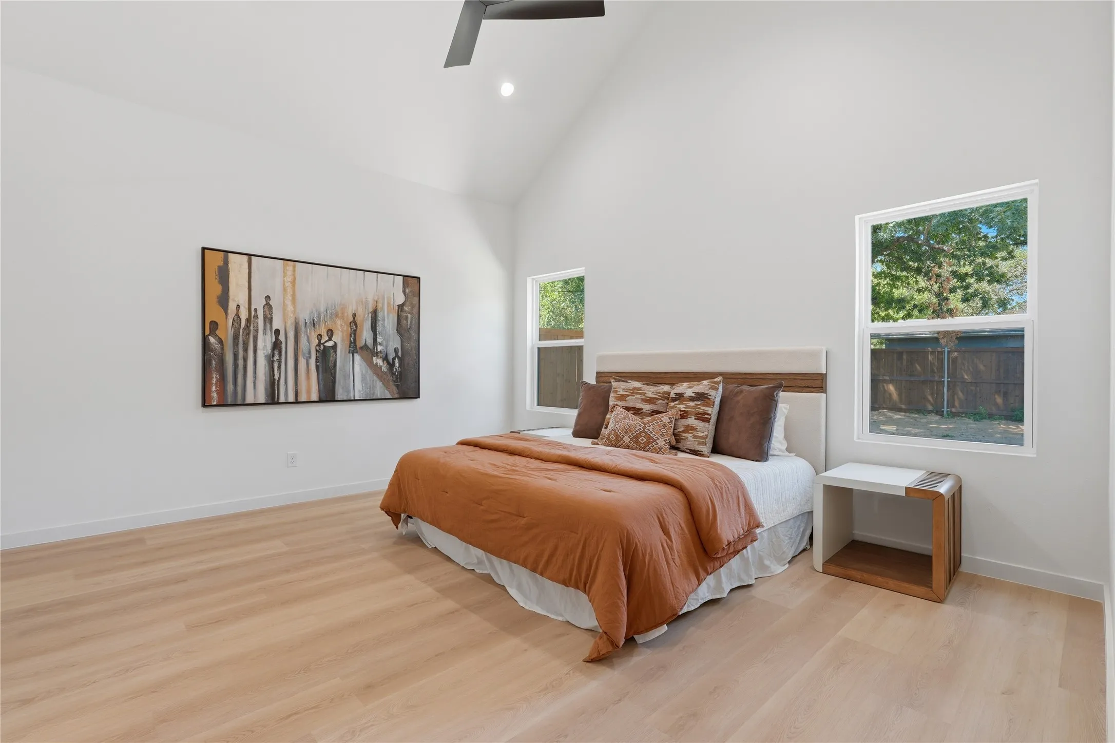 Vaulted ceiling with recessed lighting, wood-finish flooring, two large windows, and a ceiling fan