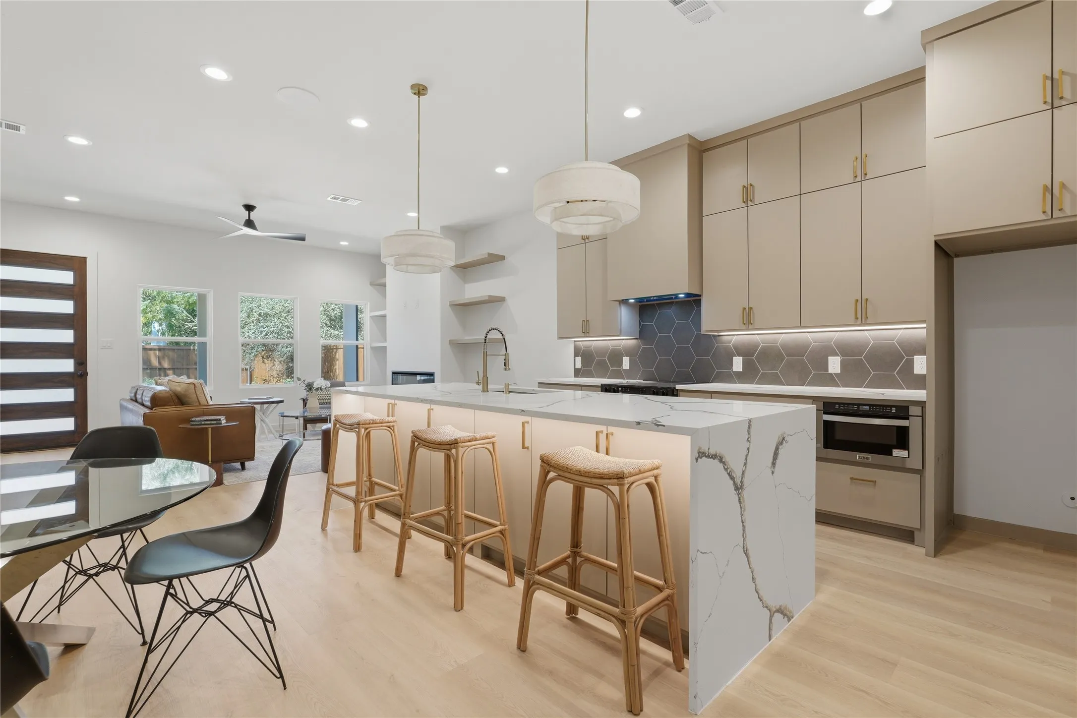 Open-concept kitchen and living area featuring a large central island with a waterfall countertop, light wood-finish flooring, and recessed lighting