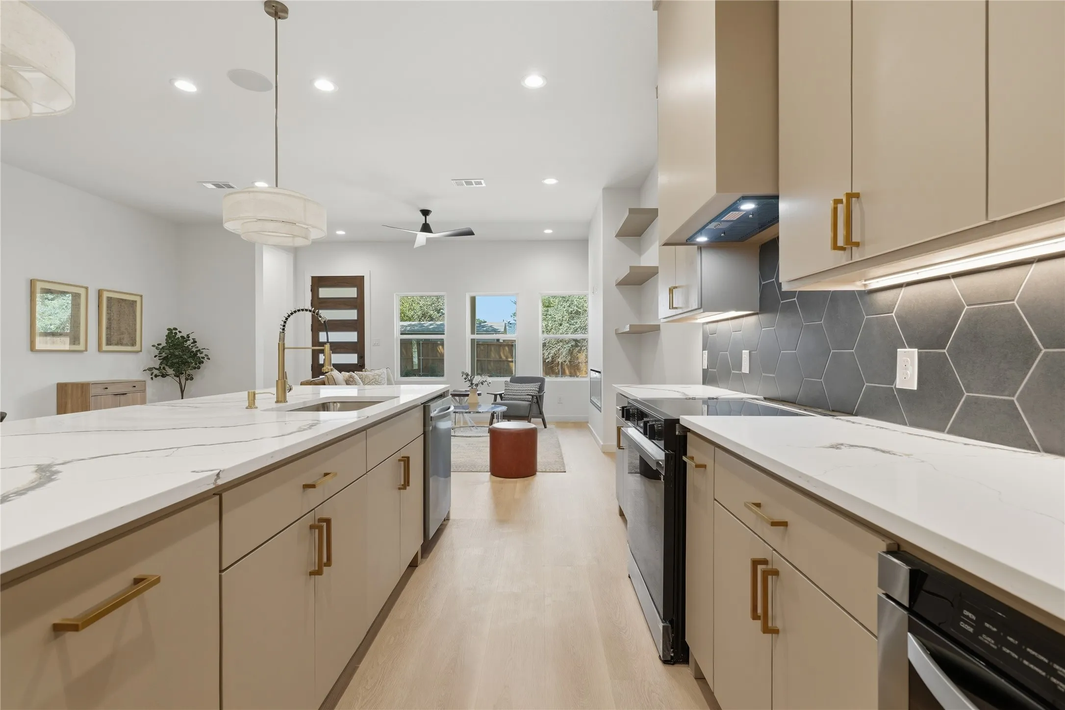 Modern kitchen with light-toned cabinetry, gold-finish hardware, white countertops, and a gray hexagonal tile backsplash