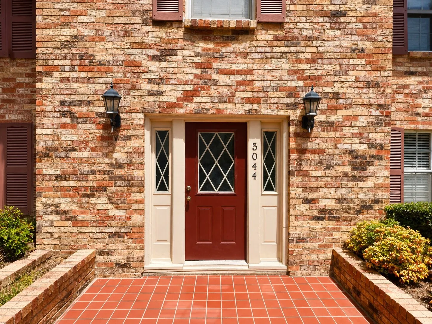 Brick facade featuring a deep red entry door with decorative glass, flanked by sidelights and outdoor sconces