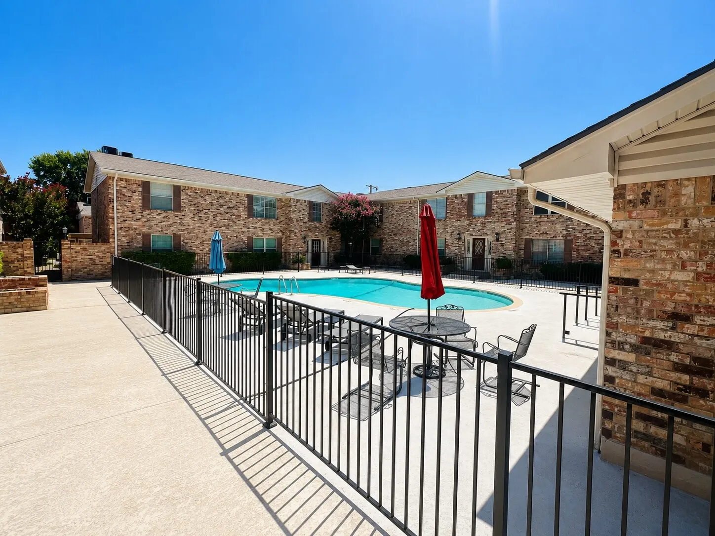 Community pool with surrounding concrete patio and black wrought iron fencing