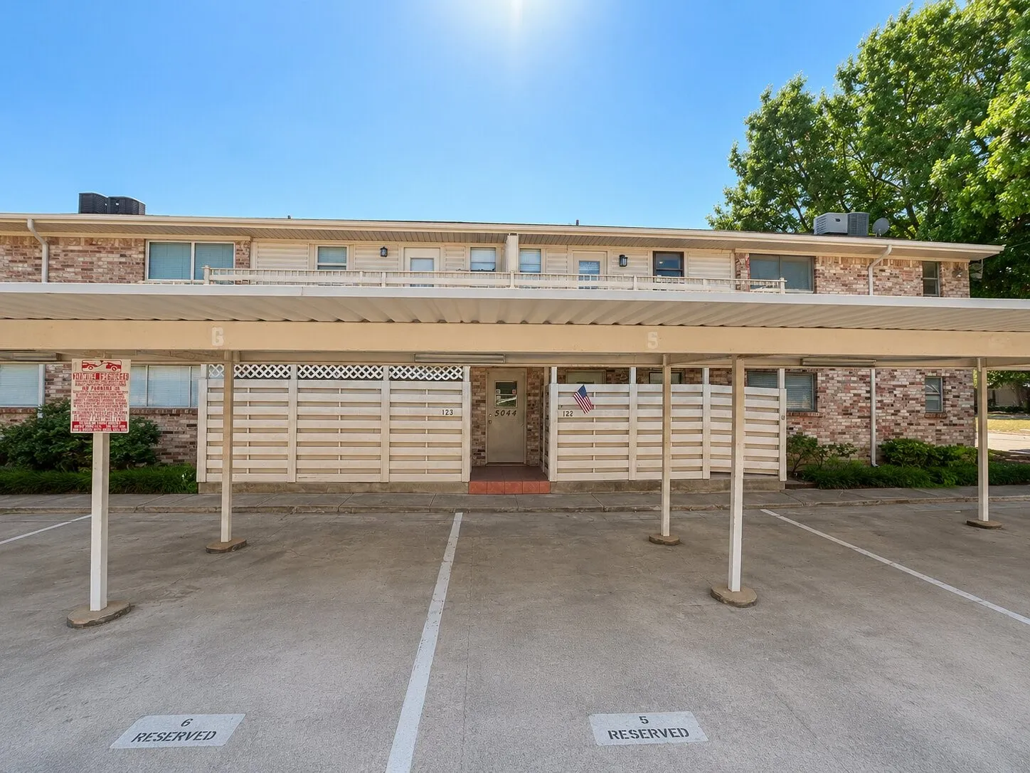 Brick exterior featuring multiple windows and a covered carport with designated parking spaces