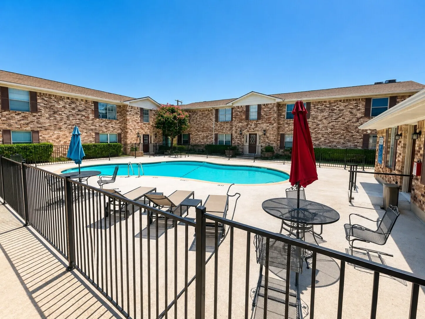 Fenced swimming pool area with concrete decking and surrounding brick buildings