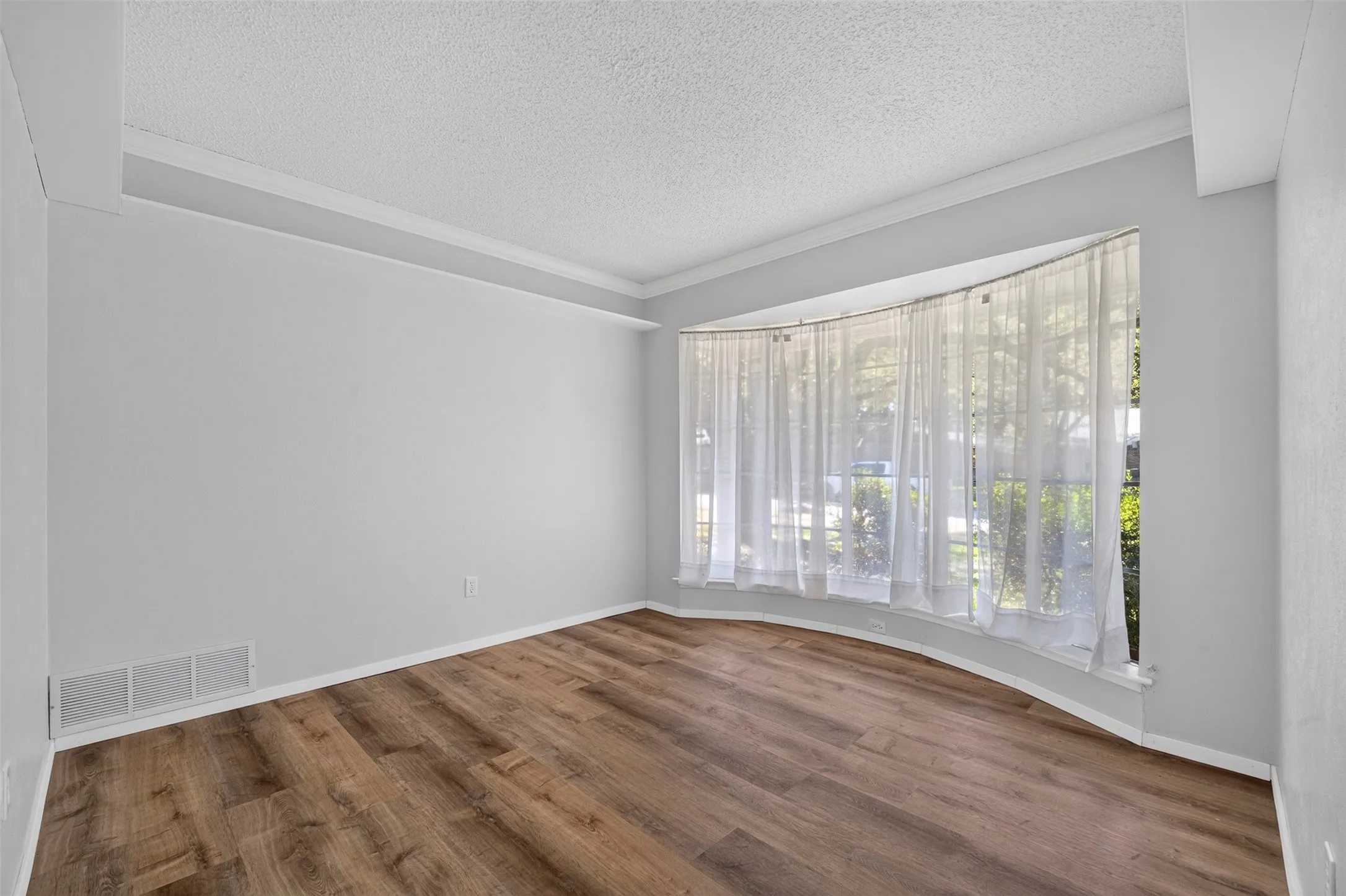 Curved bay window, wood-finish flooring, white crown molding, light-toned wall paint, and white trim