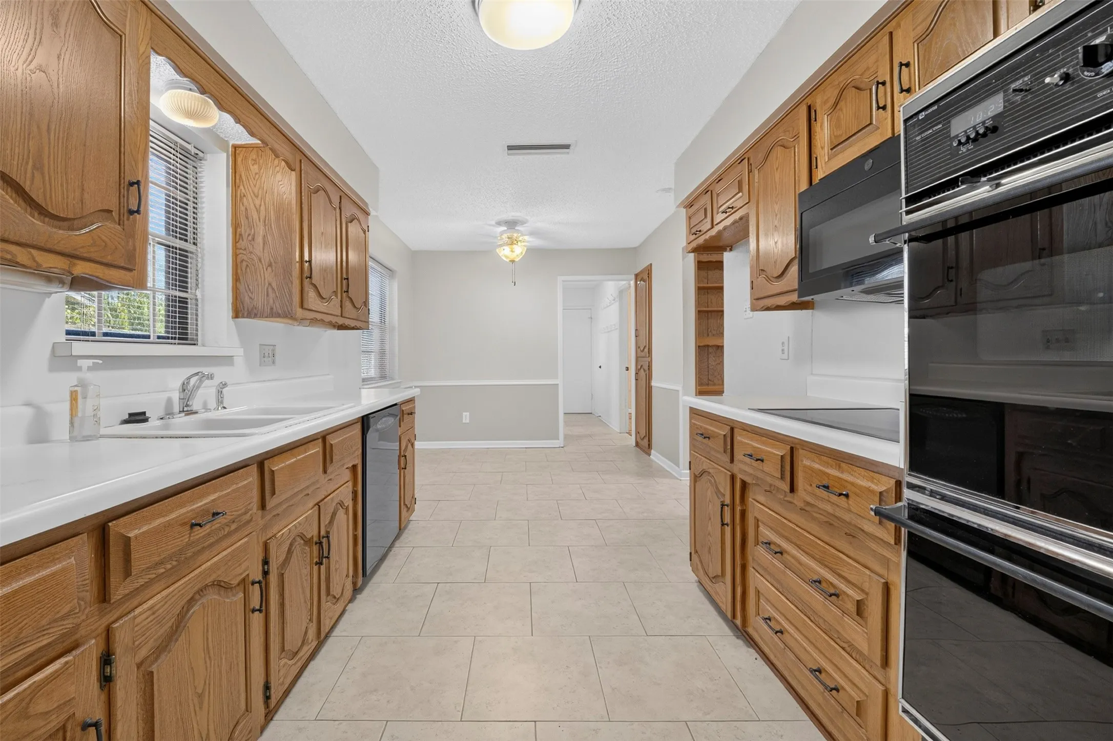 Galley kitchen featuring wood cabinetry, white countertops, a built-in microwave, and a double oven