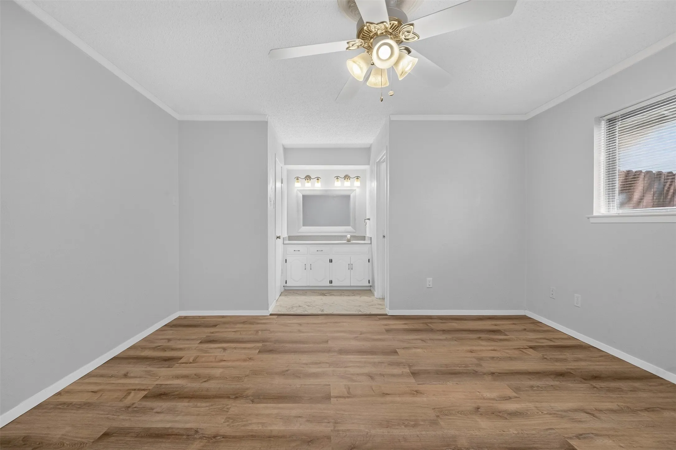 Wood-finish flooring, ceiling fan with integrated lighting, window with blinds, light gray wall paint, and white trim