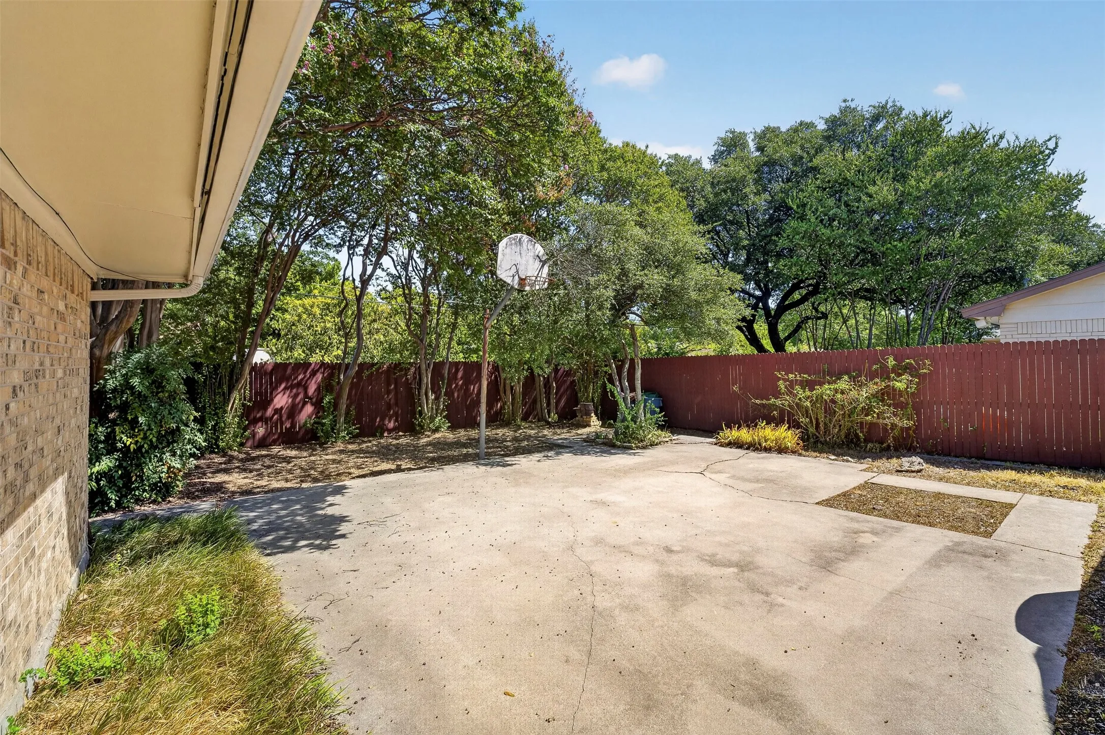 Expansive concrete patio with a basketball hoop, surrounded by mature trees and a privacy fence