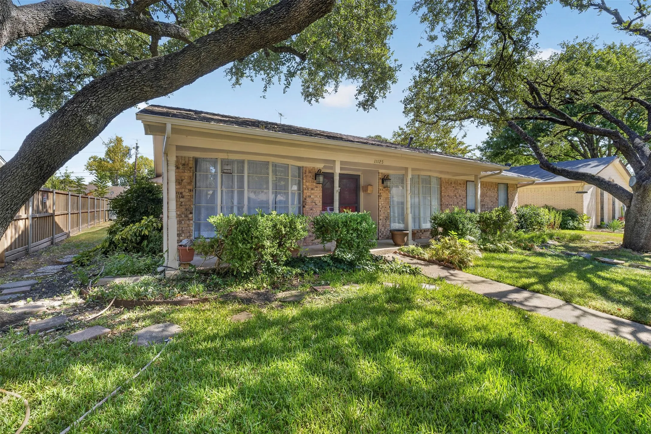 Brick facade home with mature trees, covered front porch, and a concrete walkway