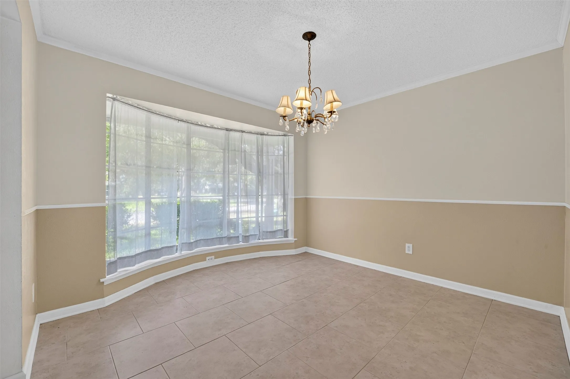 Bay window with sheer treatments, chandelier lighting fixture, neutral two-tone wall paint, and tile flooring