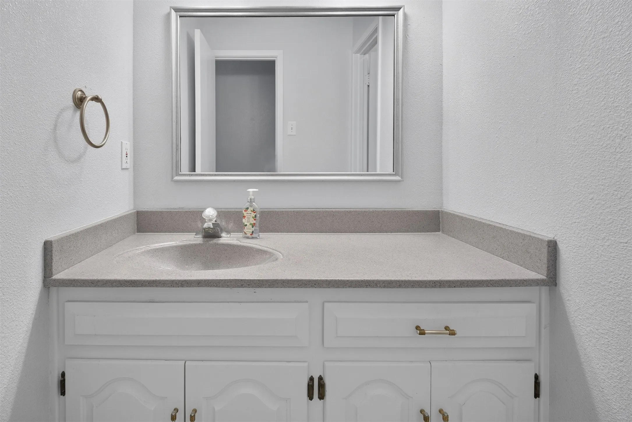 White vanity with brass hardware, integrated sink, and a framed mirror