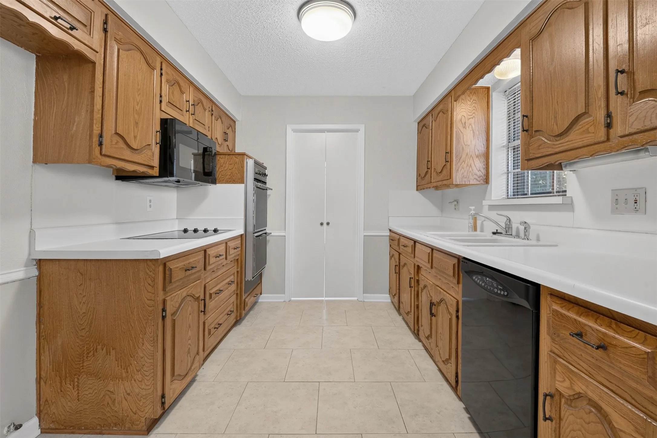 Kitchen featuring wood cabinetry, white countertops, black and stainless steel appliances, and tile flooring