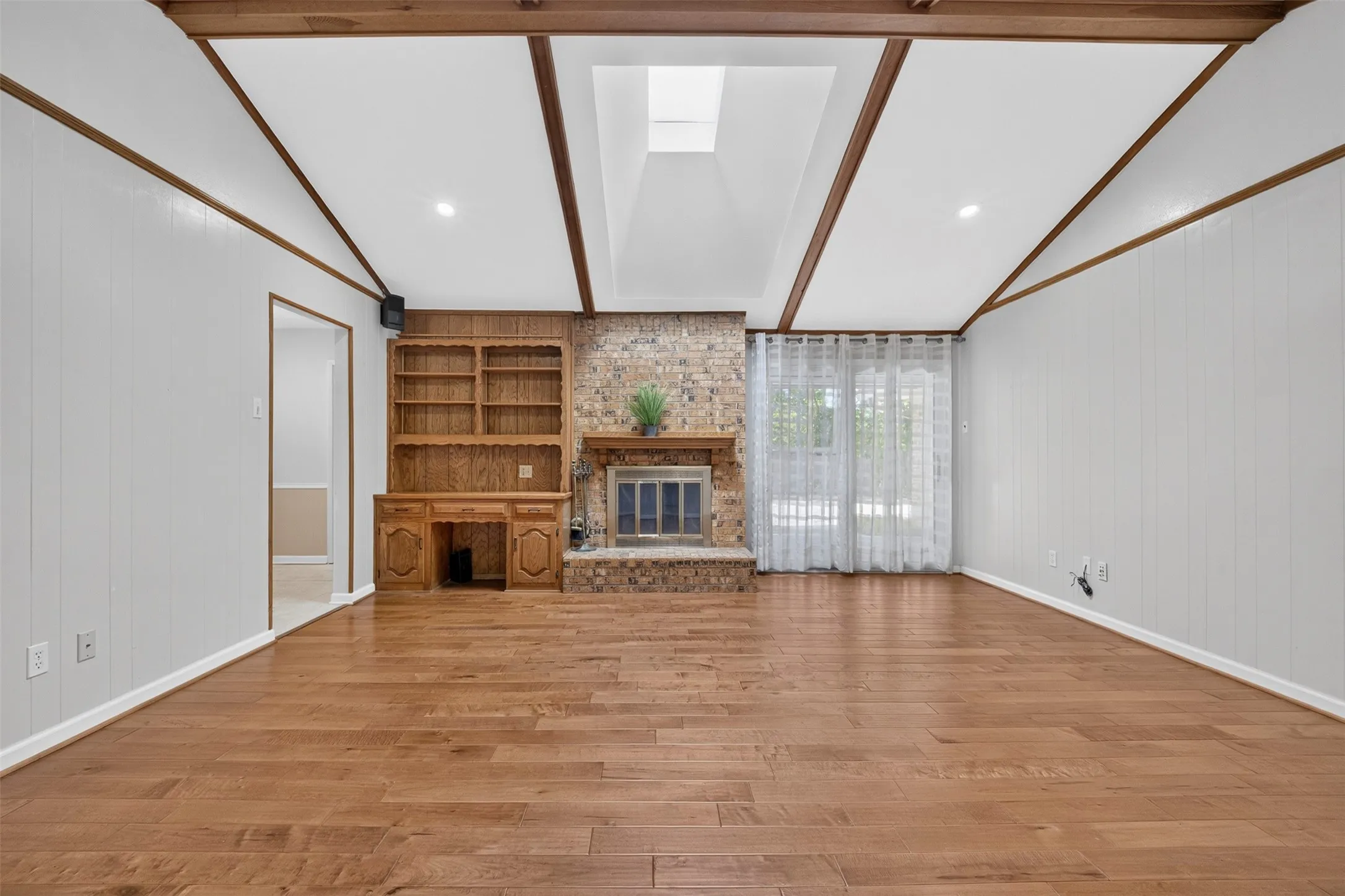 Hardwood flooring, brick fireplace, built-in shelving, exposed wood beams, and a skylight