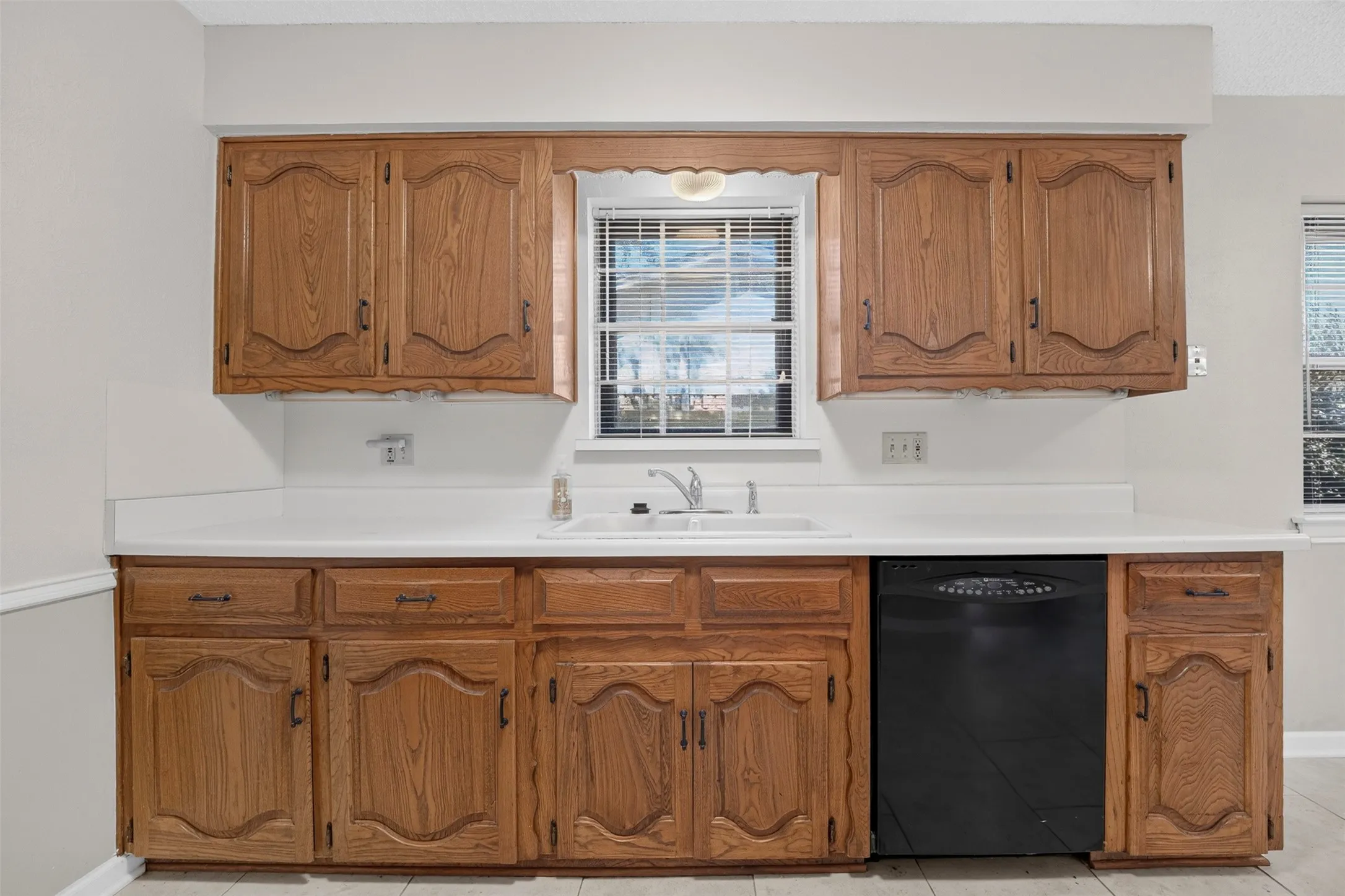 Kitchen featuring wood-finish cabinetry, white countertops, a stainless steel sink with a single-handle faucet, and a black built-in dishwasher