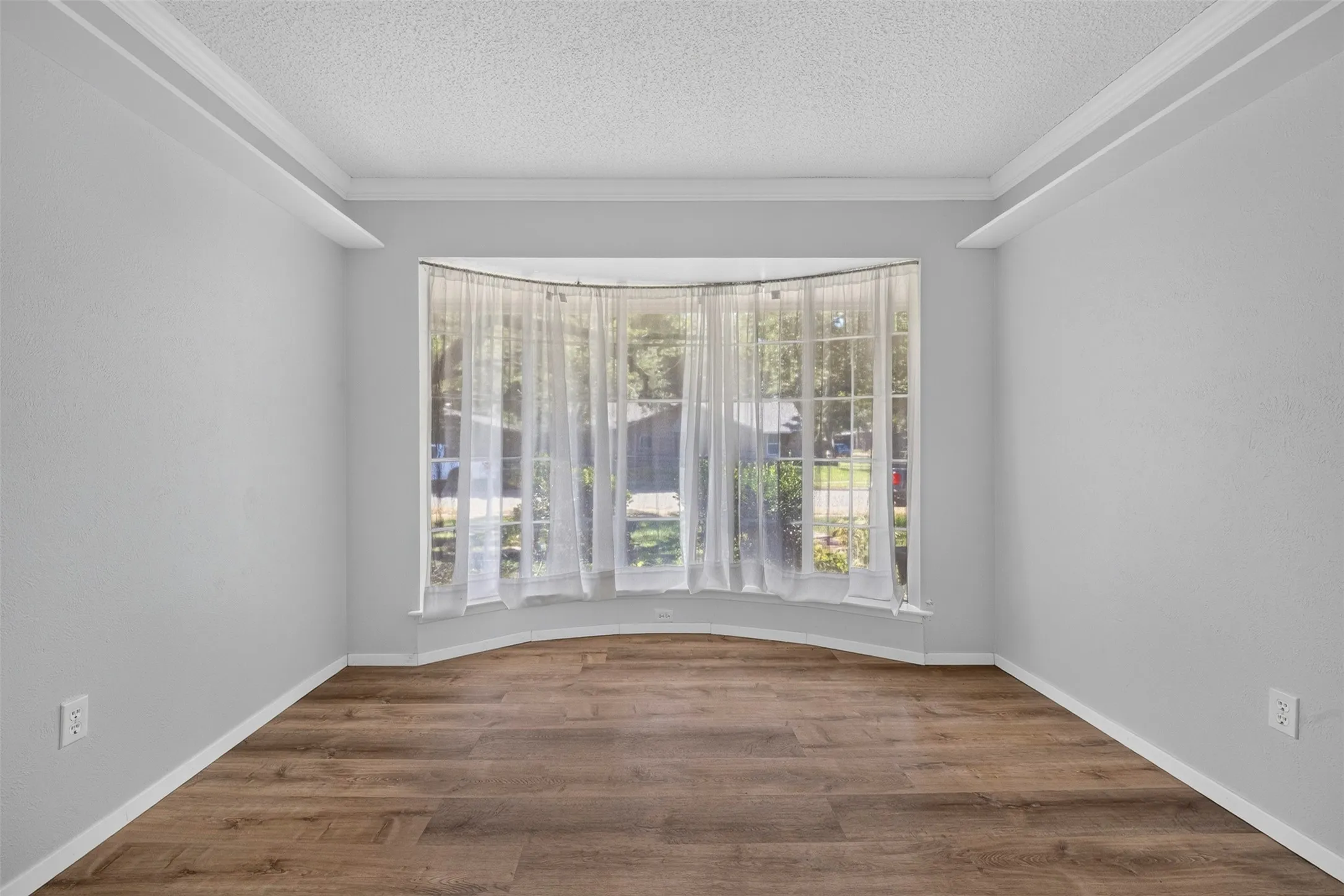 Bay window with natural light, wood-finish flooring, crown molding, and neutral wall tones