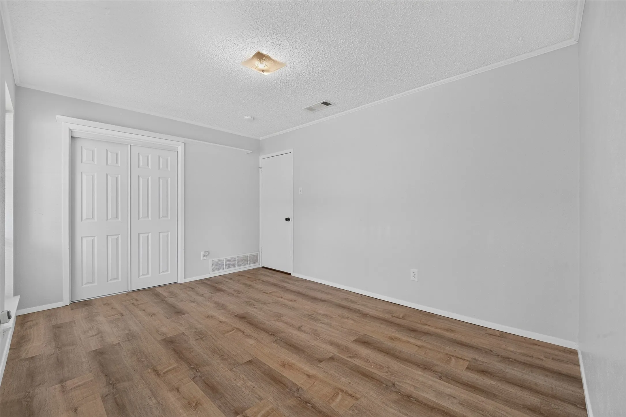 Wood-finish flooring, white paneled bifold closet doors, light neutral wall paint, and overhead flush-mount lighting