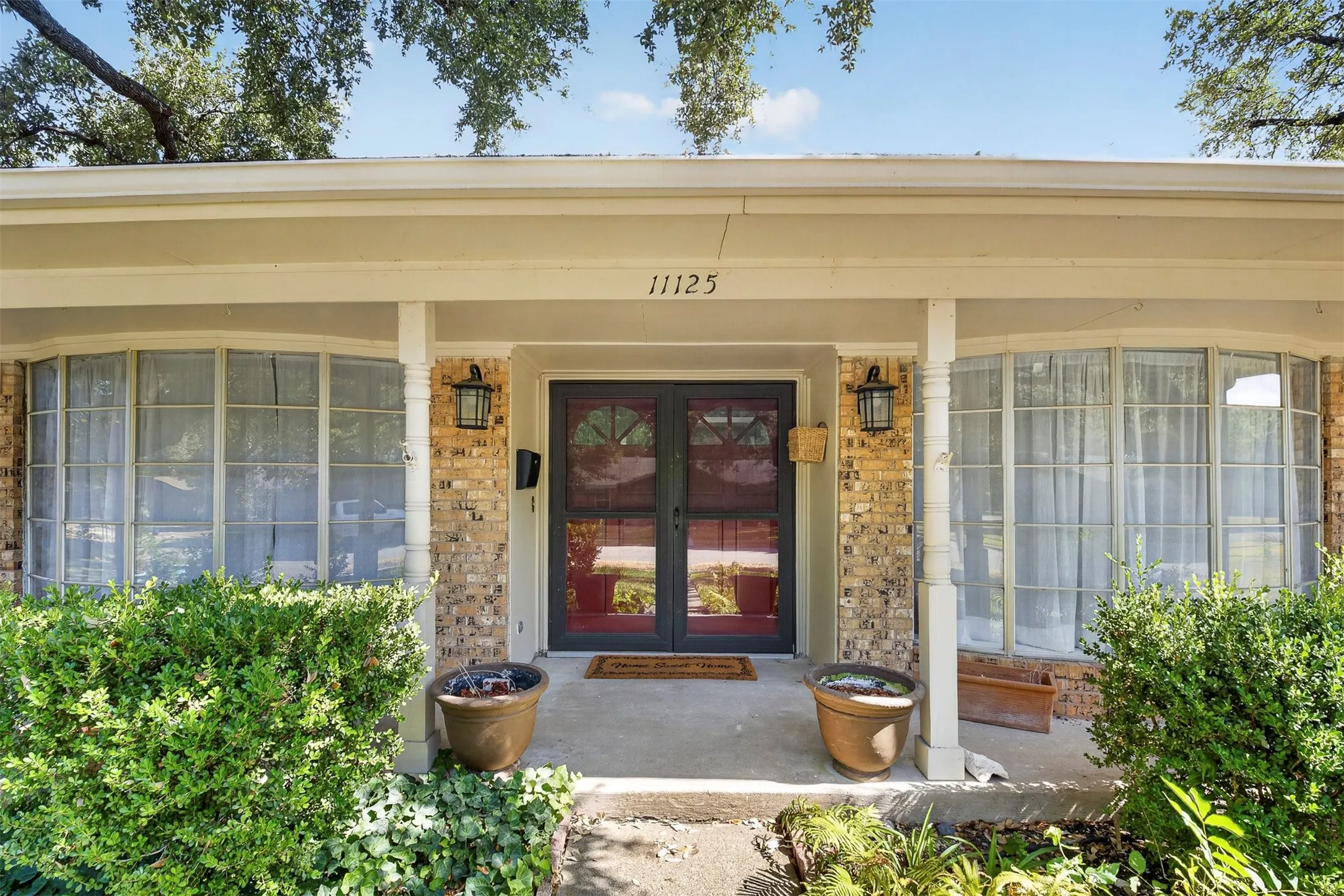Brick facade with a covered entry, dual decorative outdoor lanterns, and a dark-framed glass paneled front door
