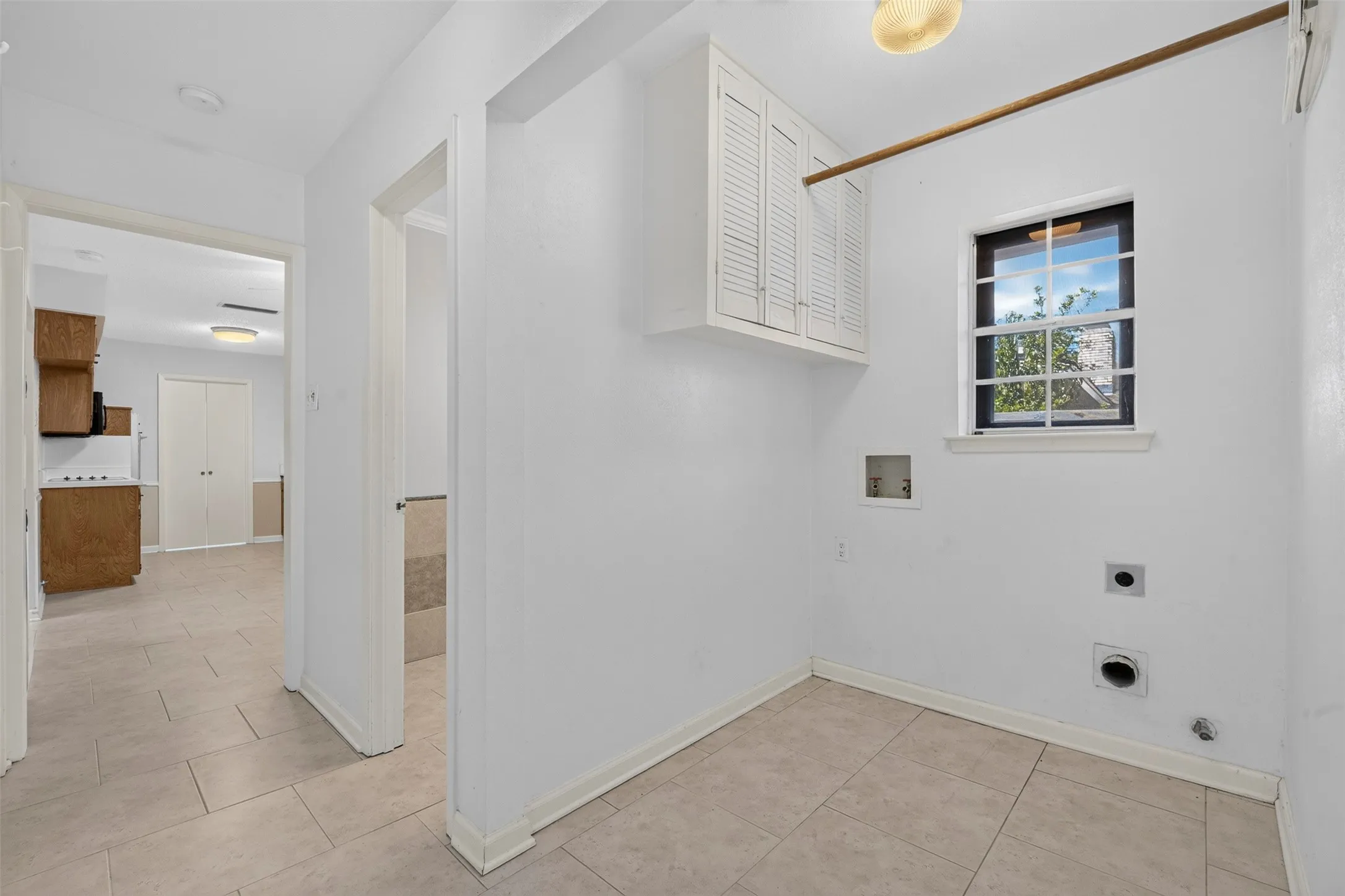 Laundry area with tiled flooring, upper cabinetry, and a window