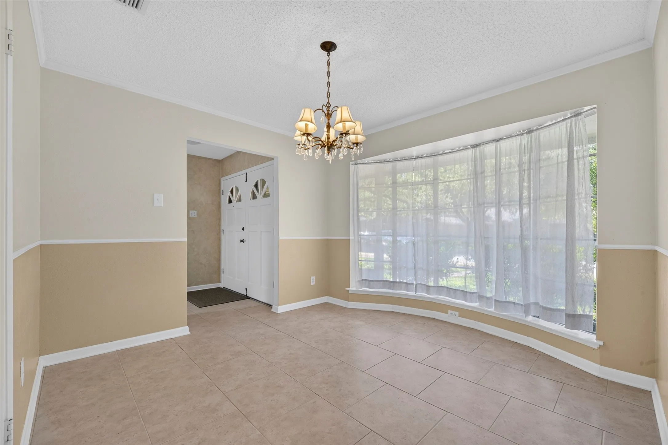 Tiled flooring, bay window with white trim, two-tone wall paint, crown molding, and a chandelier with glass accents