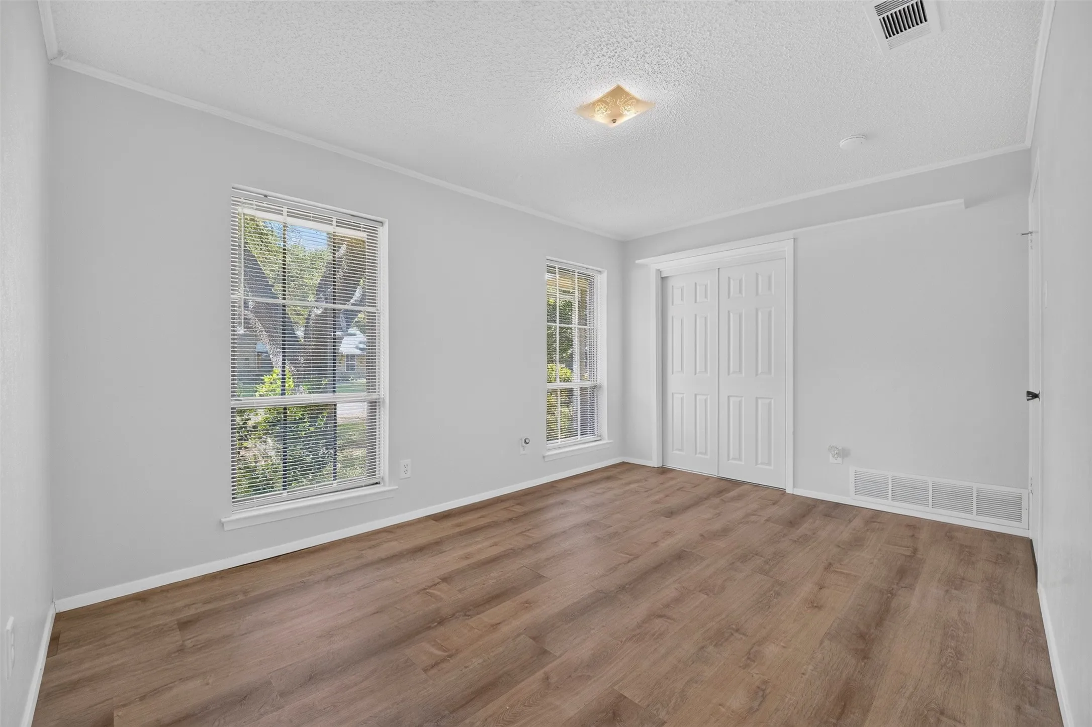 Wood-finish flooring, dual windows with blinds, bi-fold closet doors, and a ceiling-mounted light fixture