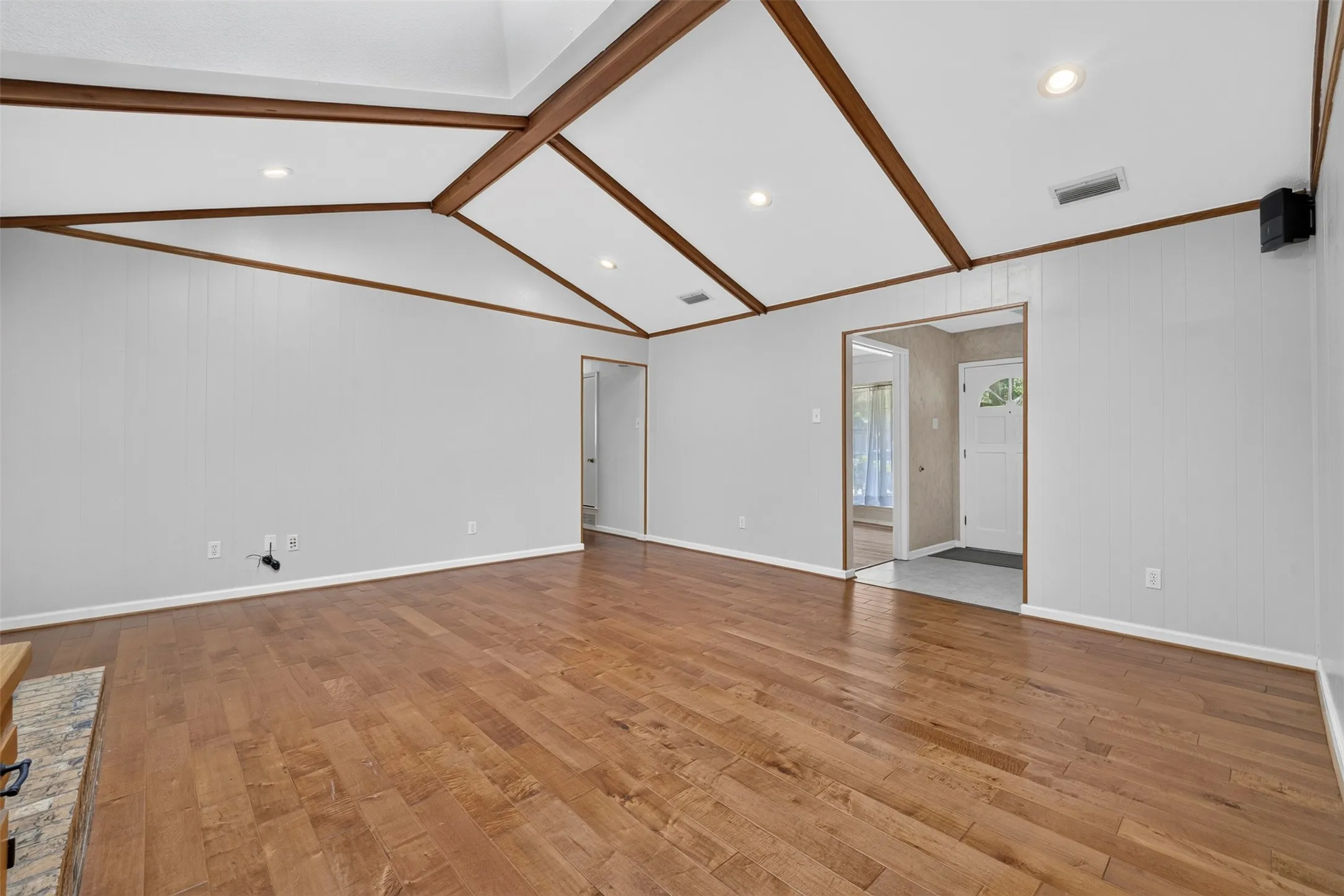 Vaulted ceiling with wood beams, recessed lighting, wood-finish flooring, and a built-in fireplace with a tile surround