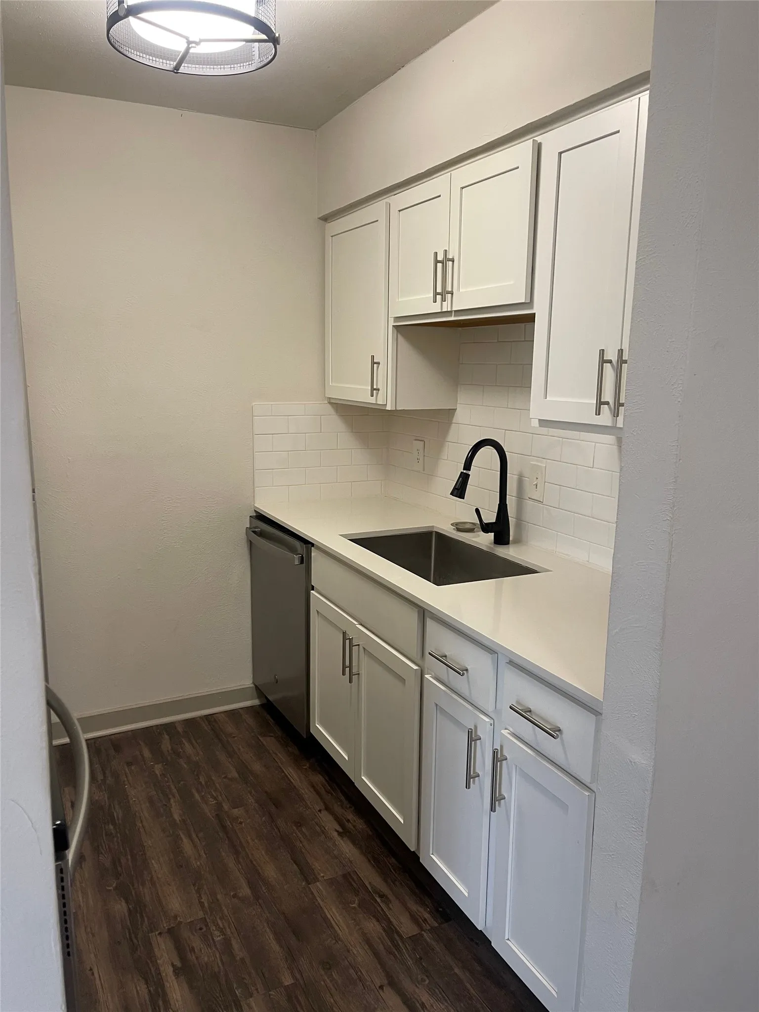 Kitchen with white shaker cabinetry, stainless steel sink, black gooseneck faucet, white subway tile backsplash, and wood-finish flooring