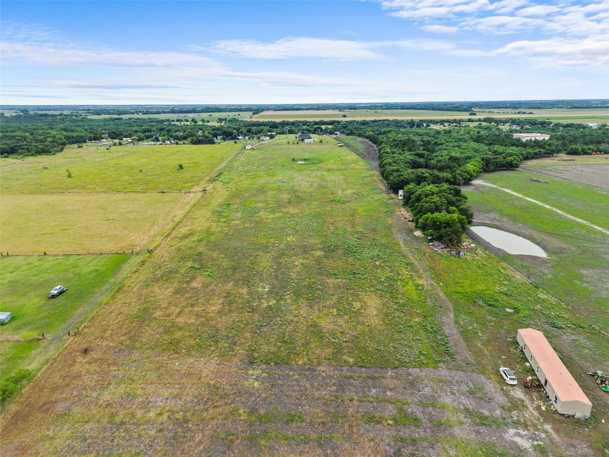 Expansive open land featuring a large pond, perimeter tree line, and a single-story outbuilding