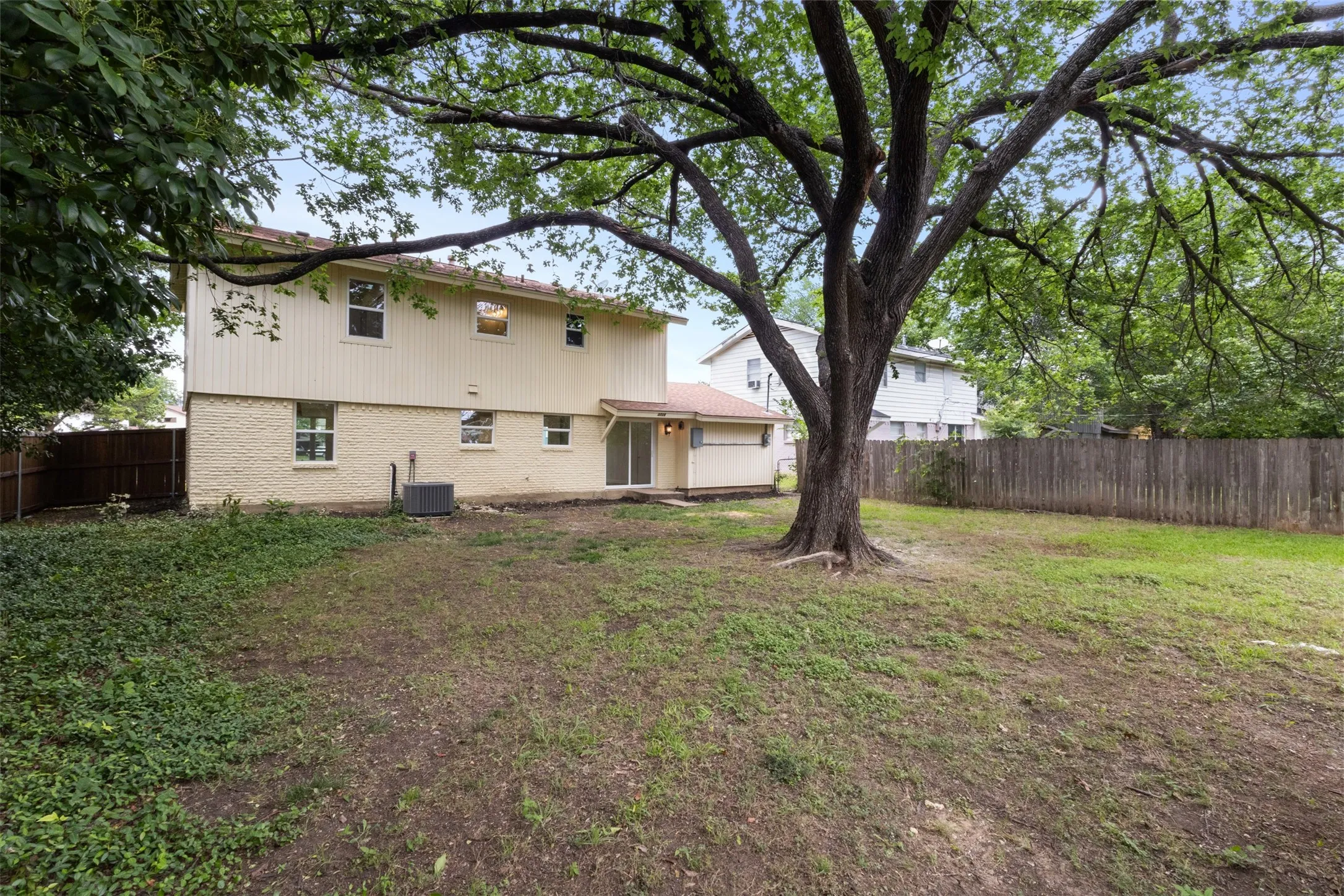 Expansive backyard featuring a mature shade tree, privacy fencing, and a two-story residence with a patio door
