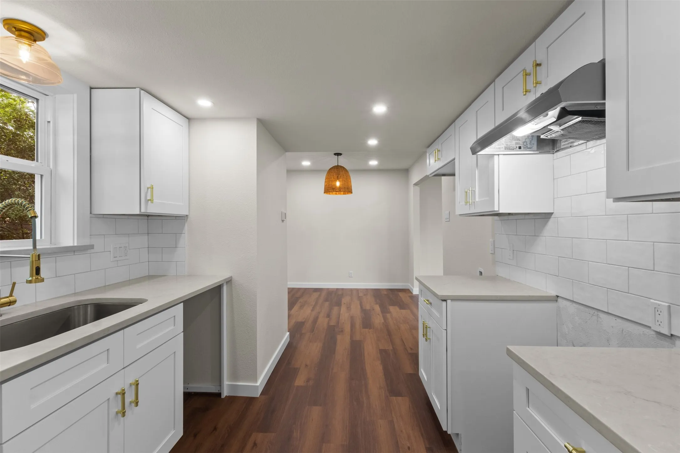 Modern kitchen featuring white shaker cabinetry, light countertops, subway tile backsplash, and wood-finish flooring