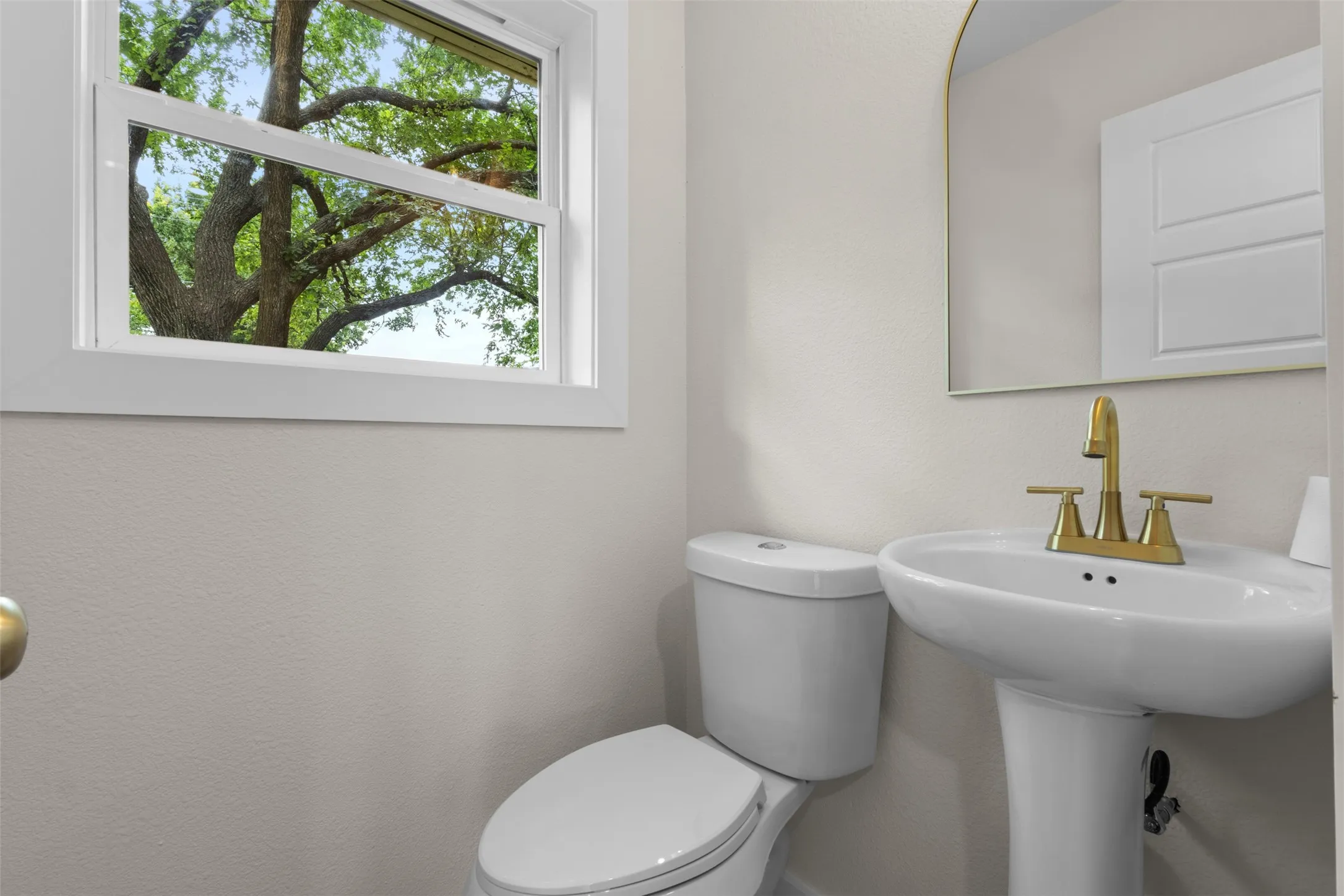 White pedestal sink with a gold-finish faucet, accompanied by a white toilet