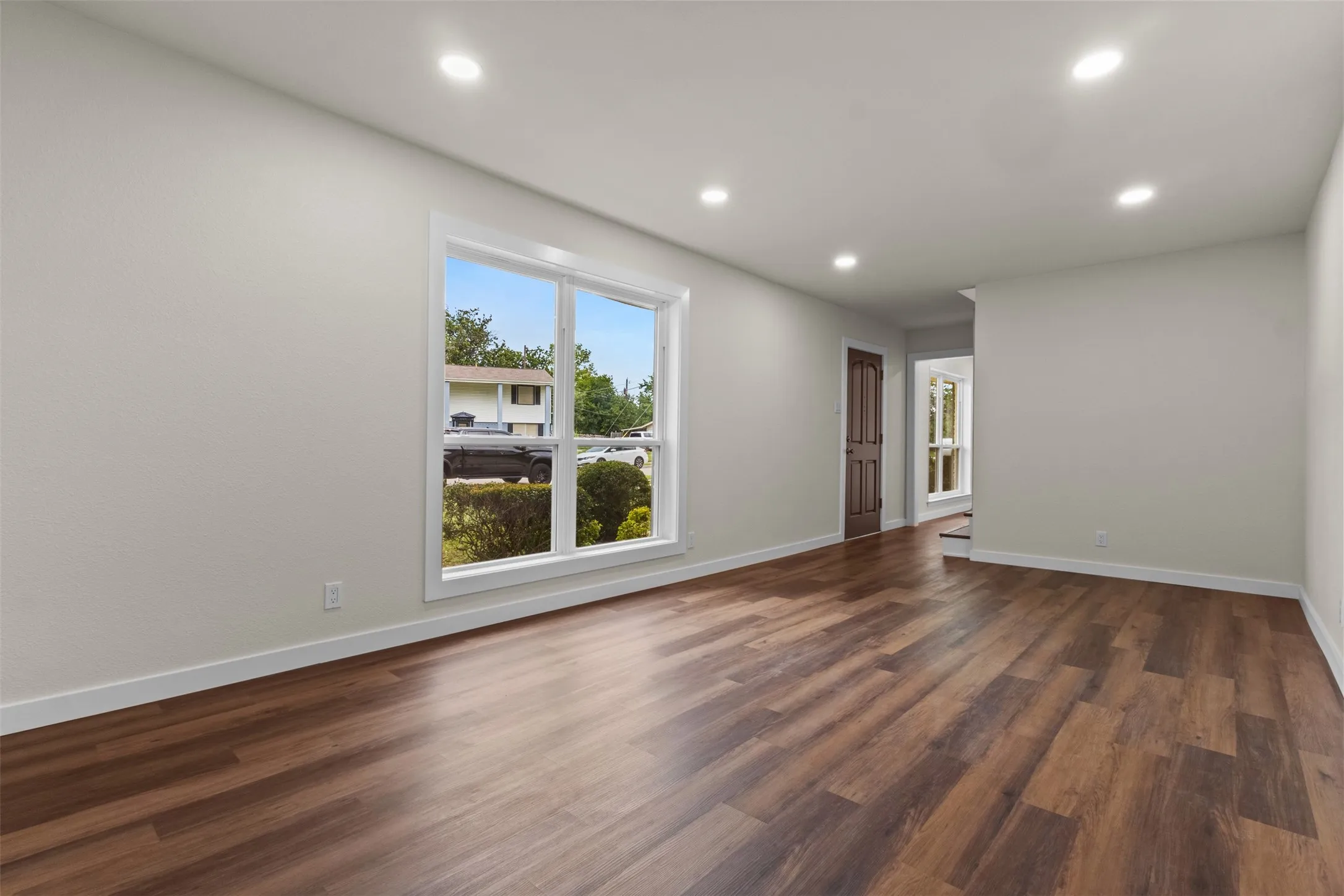 Recessed ceiling lighting, wood-finish flooring, white trim, and a paneled door