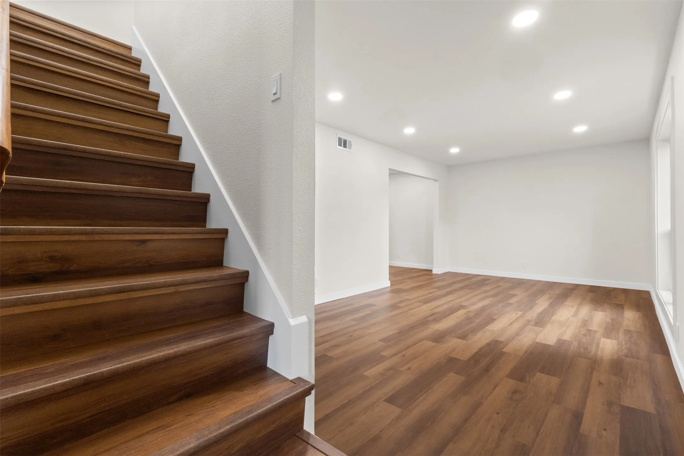 Wood-finish flooring, recessed lighting, white walls, and a wood-finish staircase