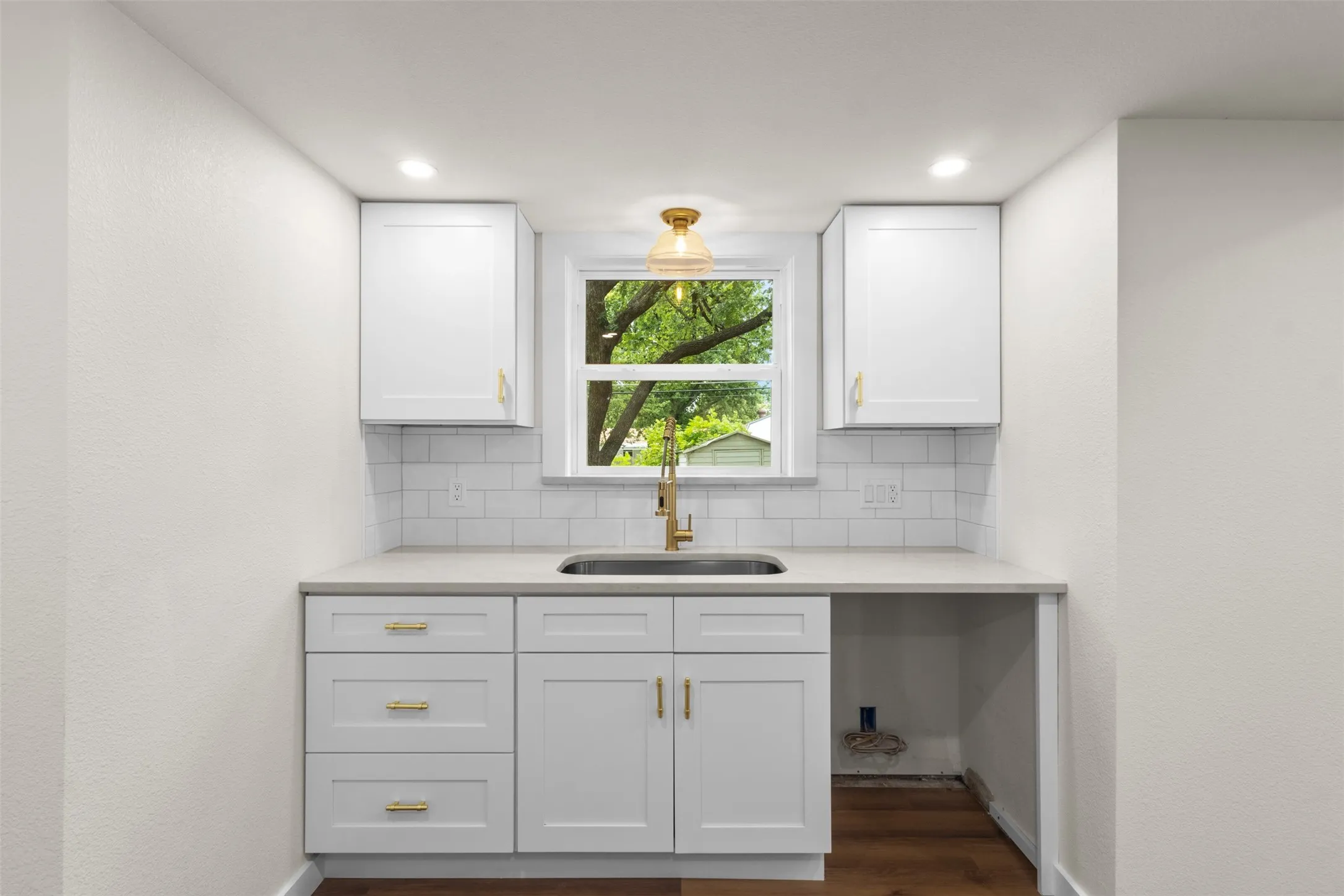 White shaker-style cabinetry with gold-tone hardware, a single basin sink, and a gold-tone faucet