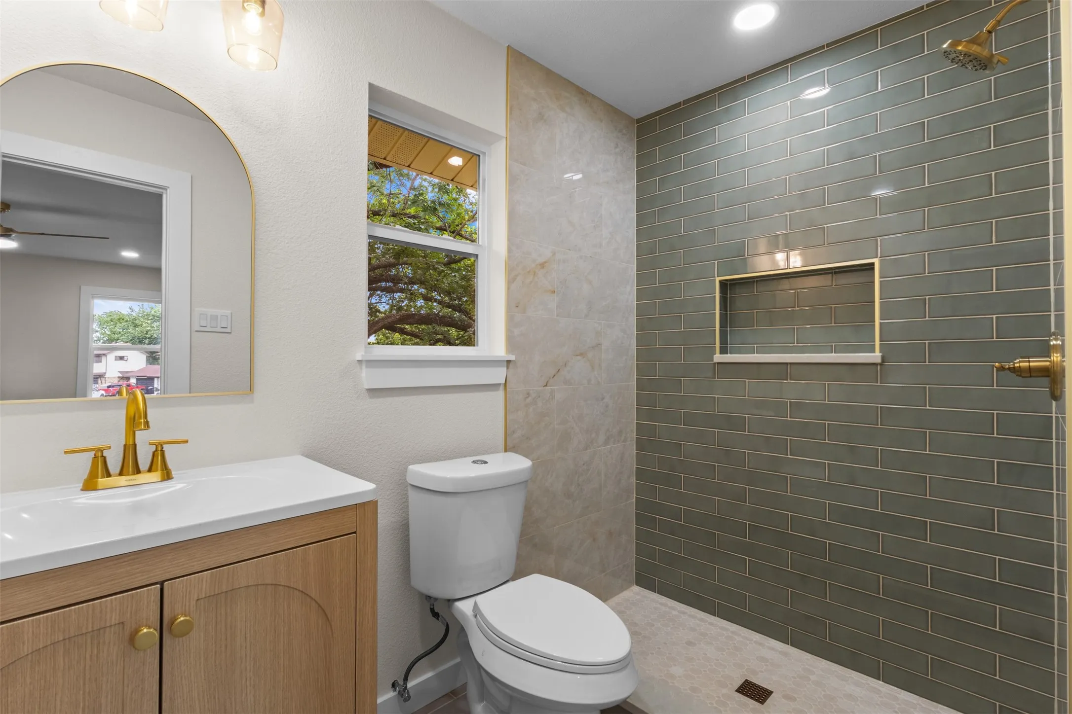 Vanity with white countertop and gold-finish faucet, arched mirror, recessed lighting, and subway tile shower with built-in niche