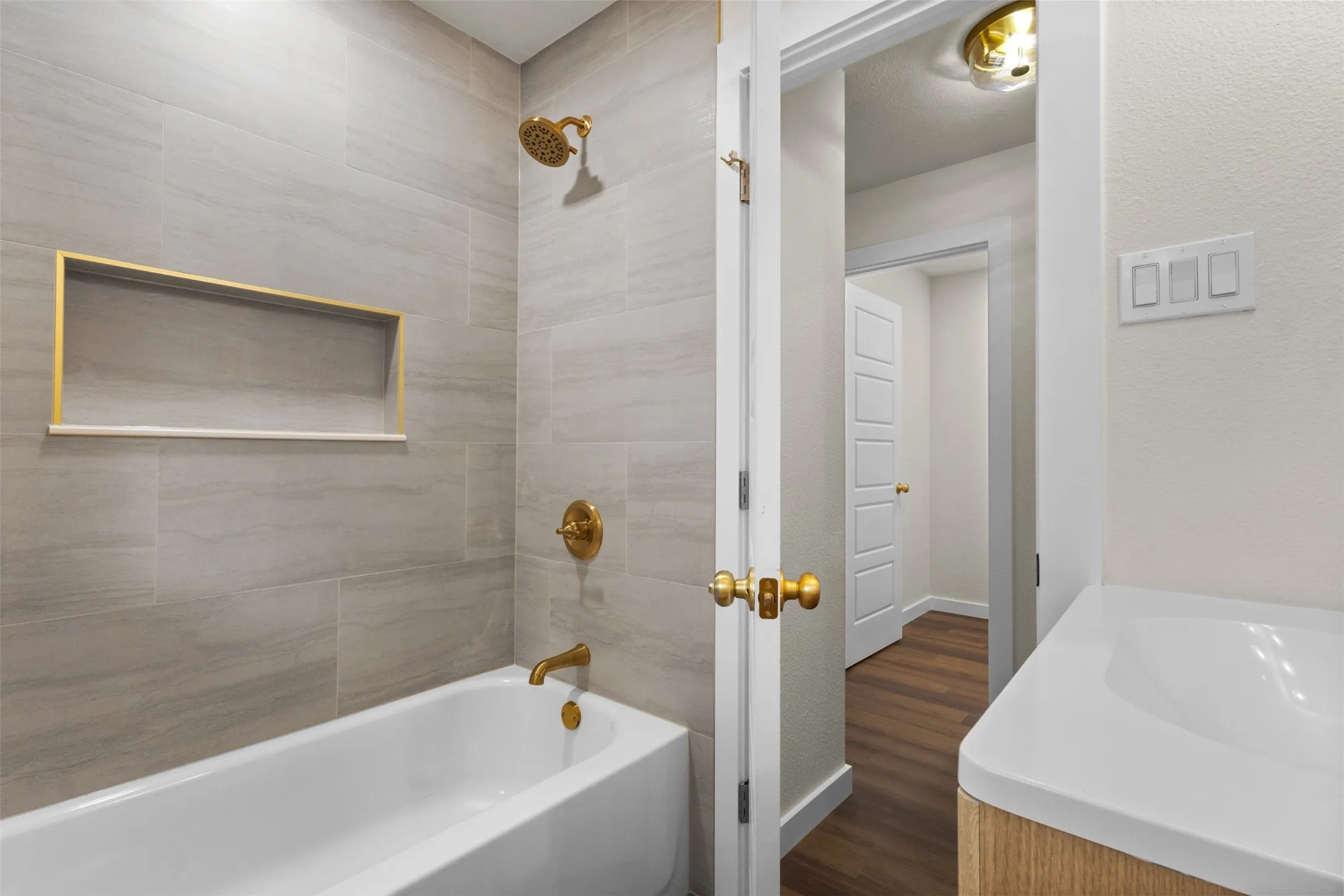 Bathtub with light-toned tiled surround, gold-finish fixtures, and a recessed shower niche