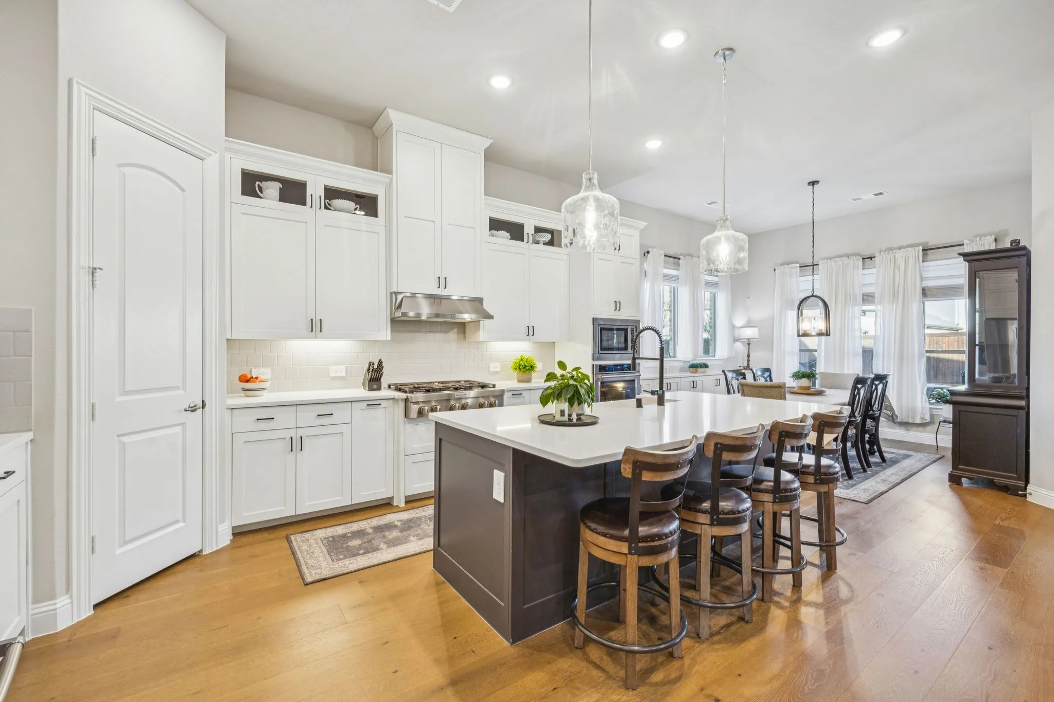 Gourmet Kitchen Featuring A Six-Burner Gas Range, Vent Hood, And Shaker Cabinetry With Curio-Style Upper Cabinets