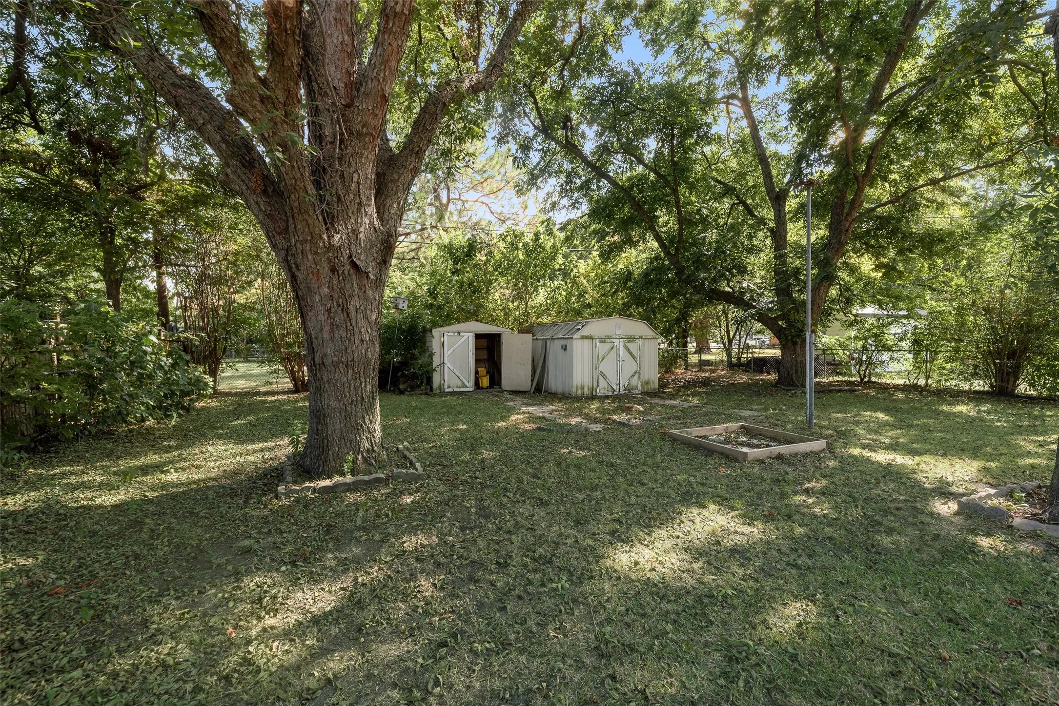 Expansive yard with mature trees, two storage sheds, and a raised garden bed