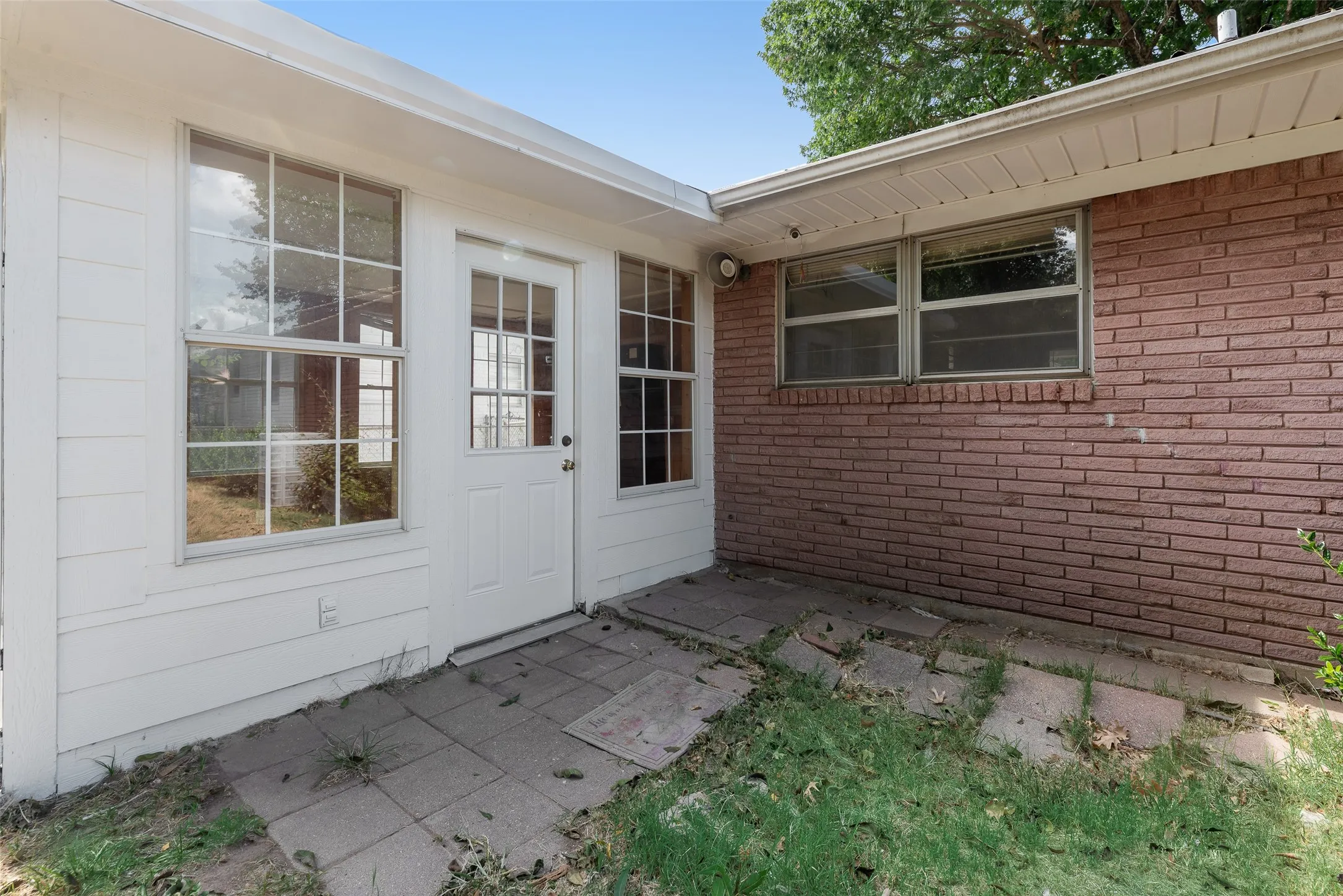 White siding, brick exterior, multiple windows, exterior door, paved patio