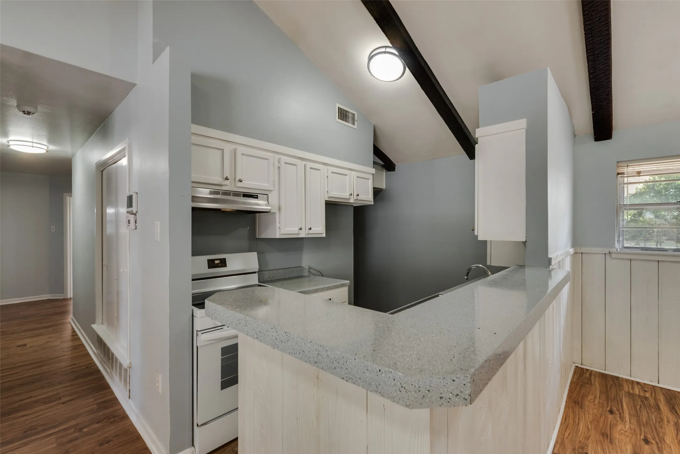 Kitchen featuring white cabinetry, gray countertop, white appliances, and exposed ceiling beams
