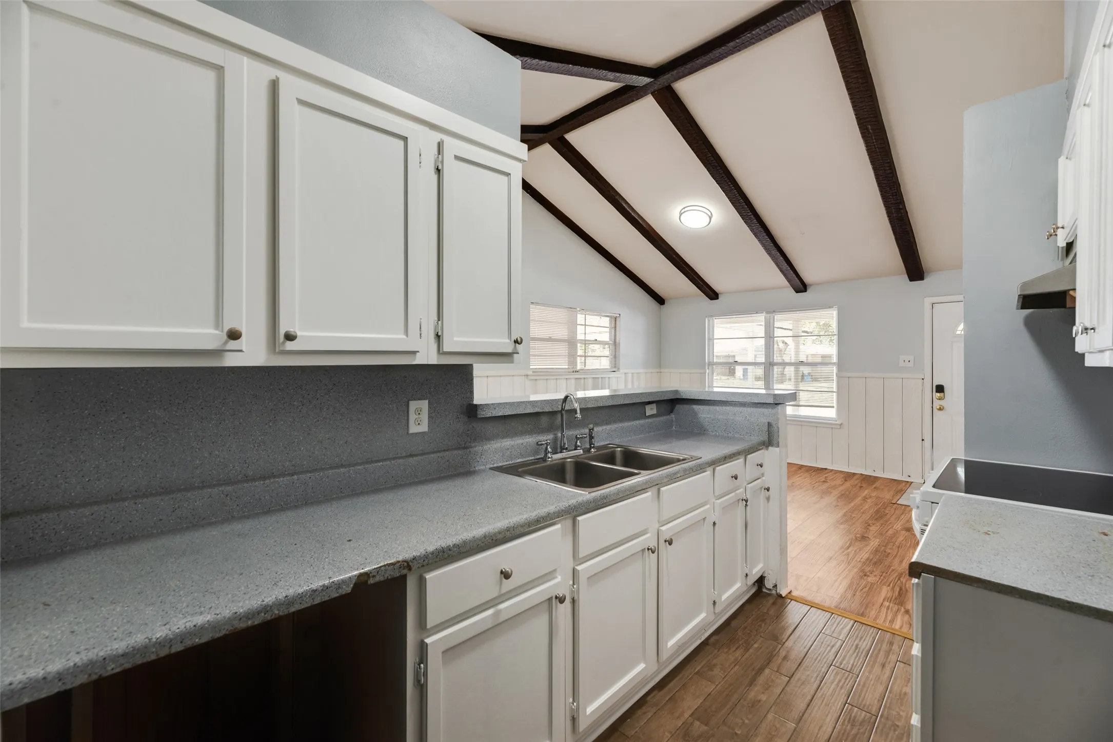 Kitchen featuring white cabinetry, gray countertops, a double basin sink, and a vaulted ceiling with exposed beams