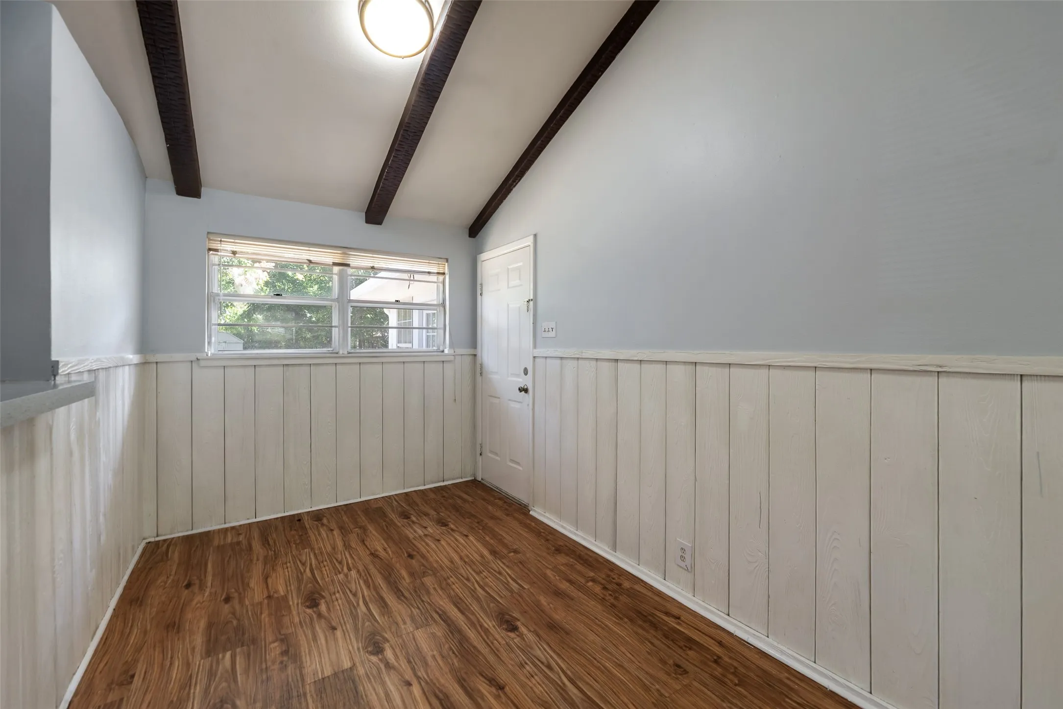 Vaulted ceiling with exposed beams, wood-finish flooring, and white paneled wainscoting