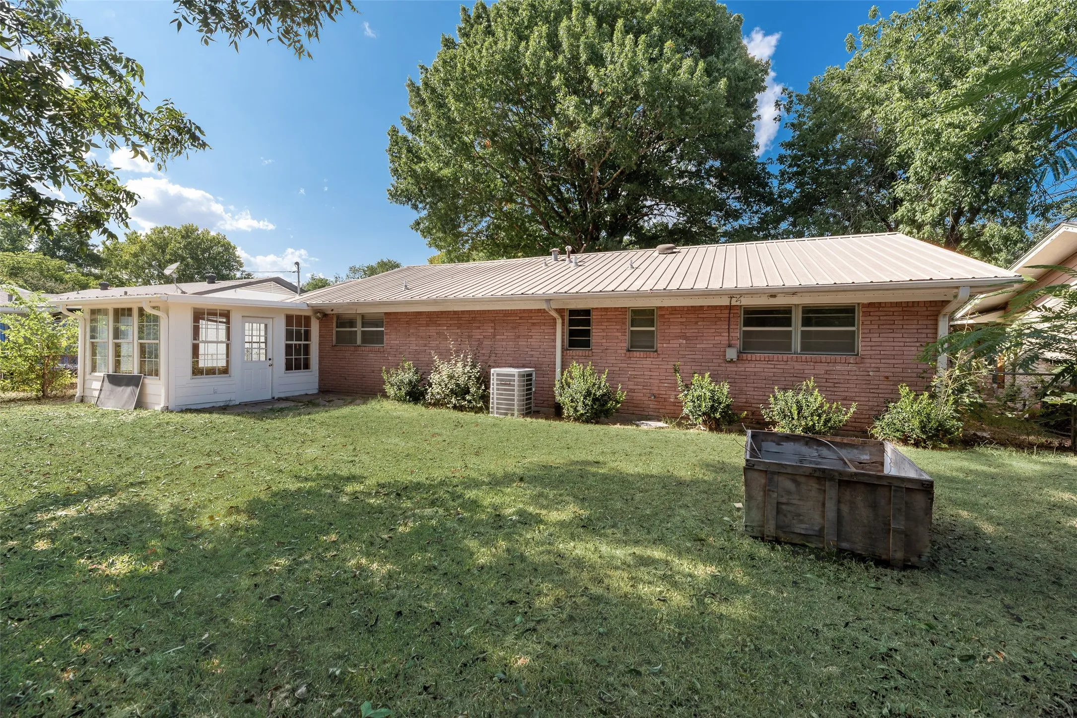Brick exterior with a metal roof, featuring a sunroom addition with multiple windows and a white exterior door