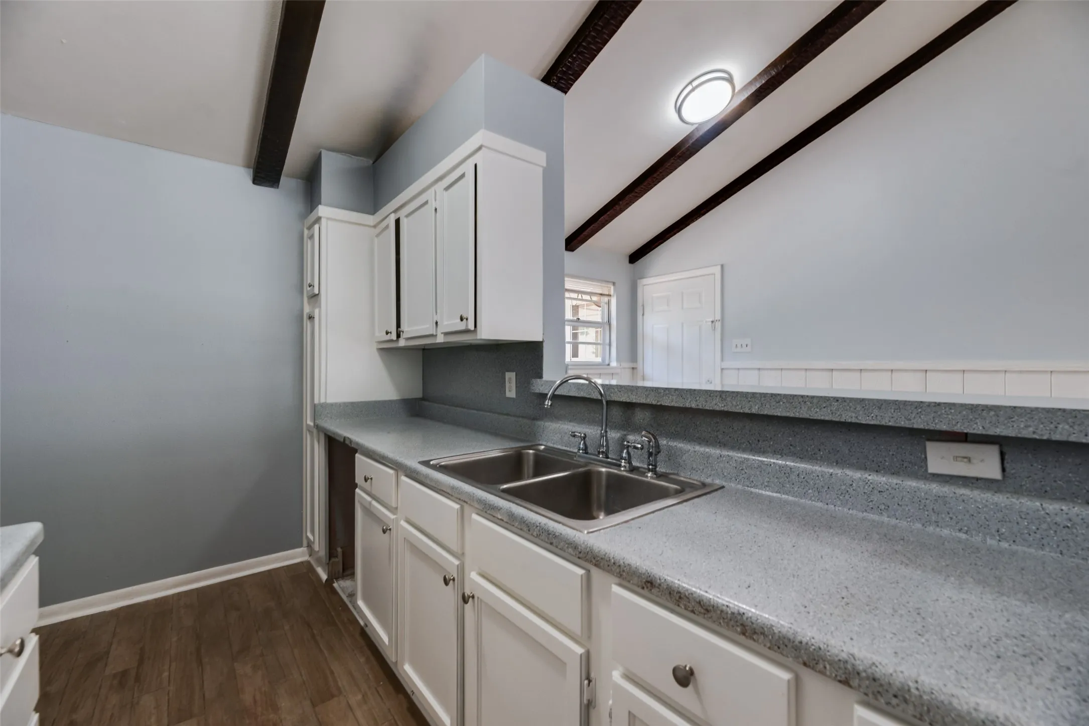 Kitchen featuring white cabinetry, a dual basin stainless steel sink, speckled countertops, and wood-finish flooring
