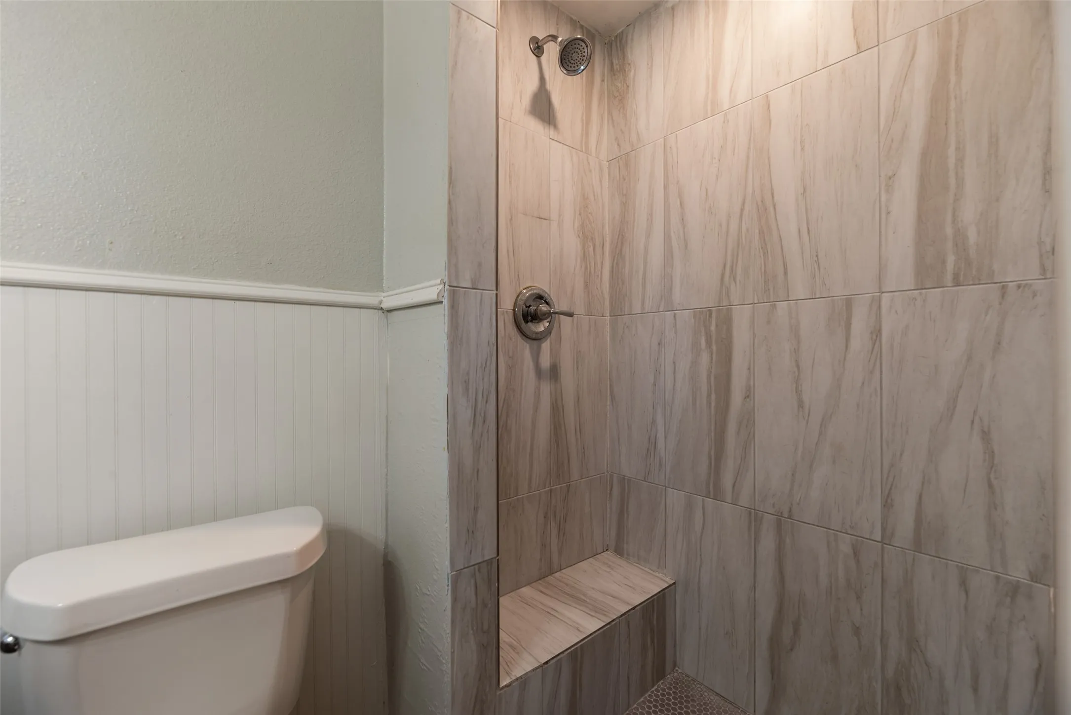 Tiled shower with a built-in bench, wall-mounted showerhead, and a coordinating shower control