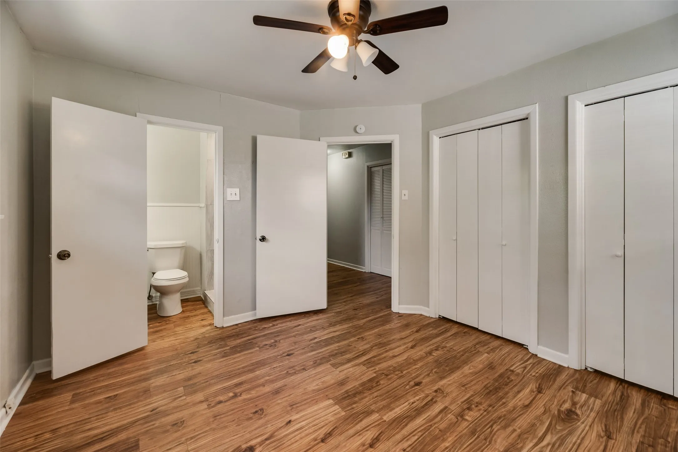 Wood-finish flooring, ceiling fan with integrated lighting, multiple bi-fold closet doors, and light-toned wall paint