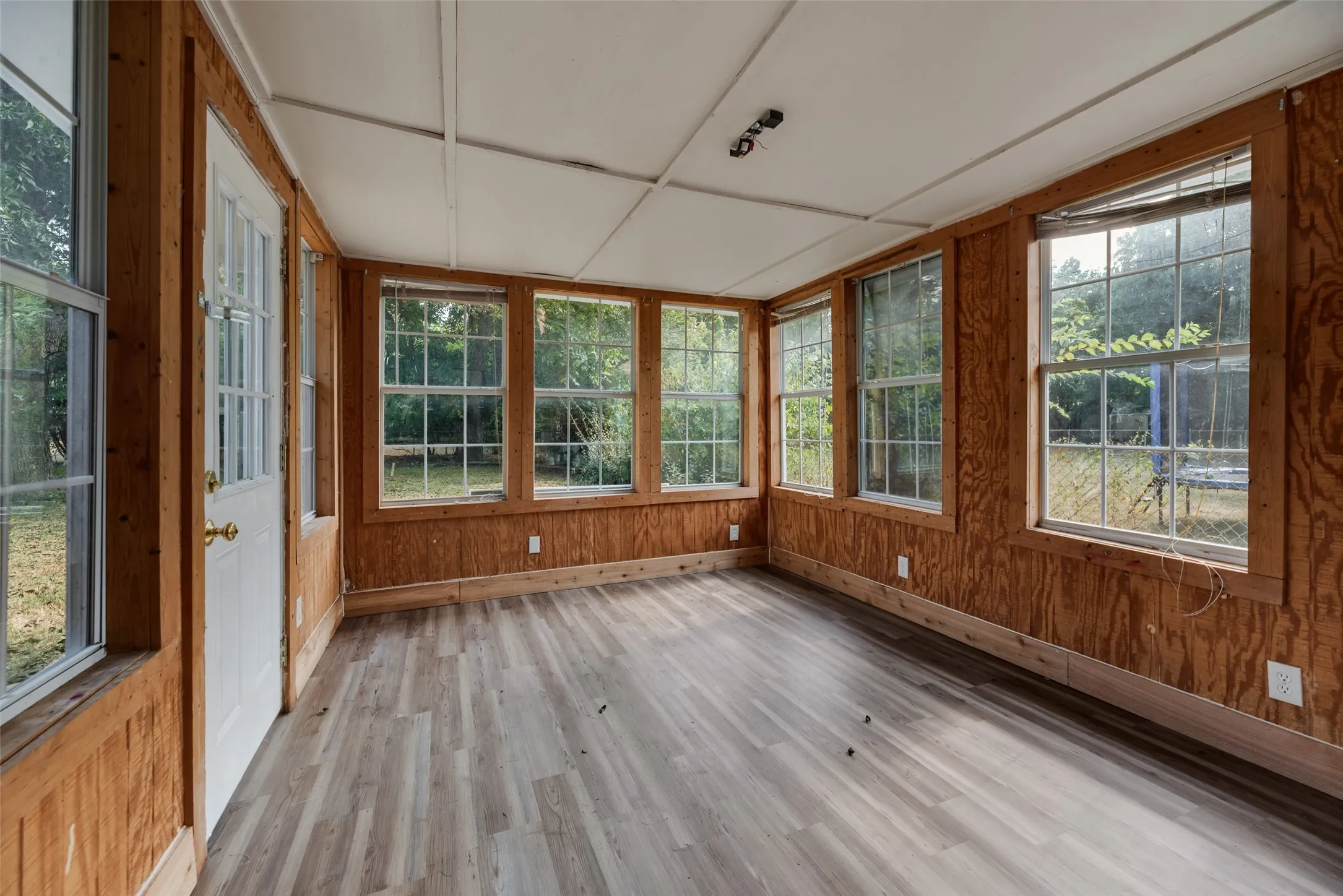 Sunroom featuring light wood-finish flooring, wood paneling, and multiple transom windows